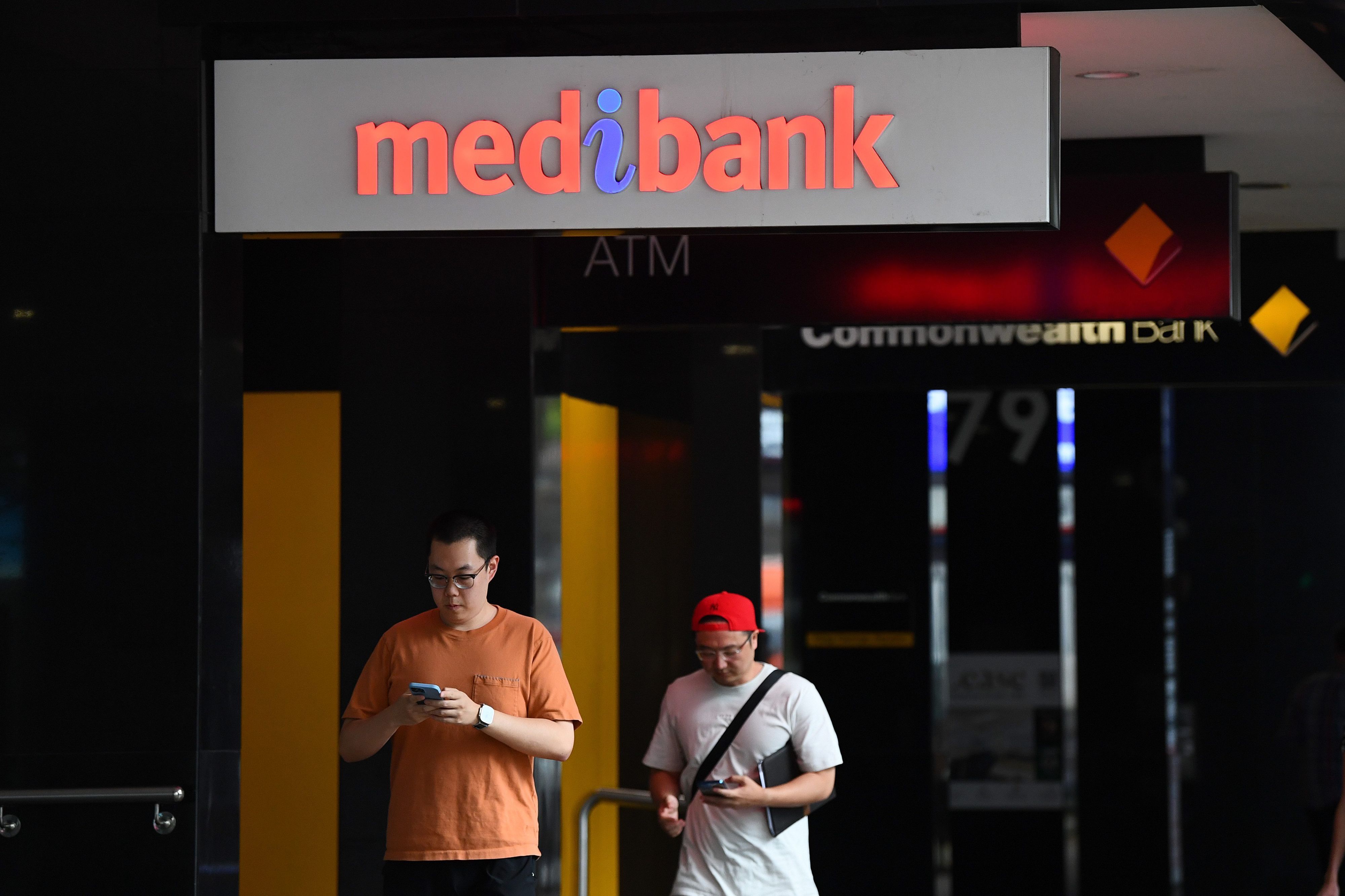 Passanten laufen an einem Medibank-Schild vorbei. Sie haben Handys in der Hand.