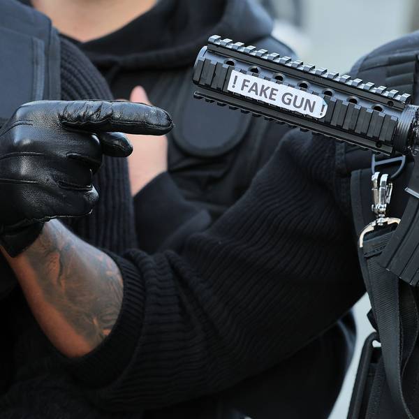 Ein als Swat-Polizist verkleideter Karnevalist hält eine Pistolenattrappe mit der Aufschrift „Fake Gun“ in der Hand.