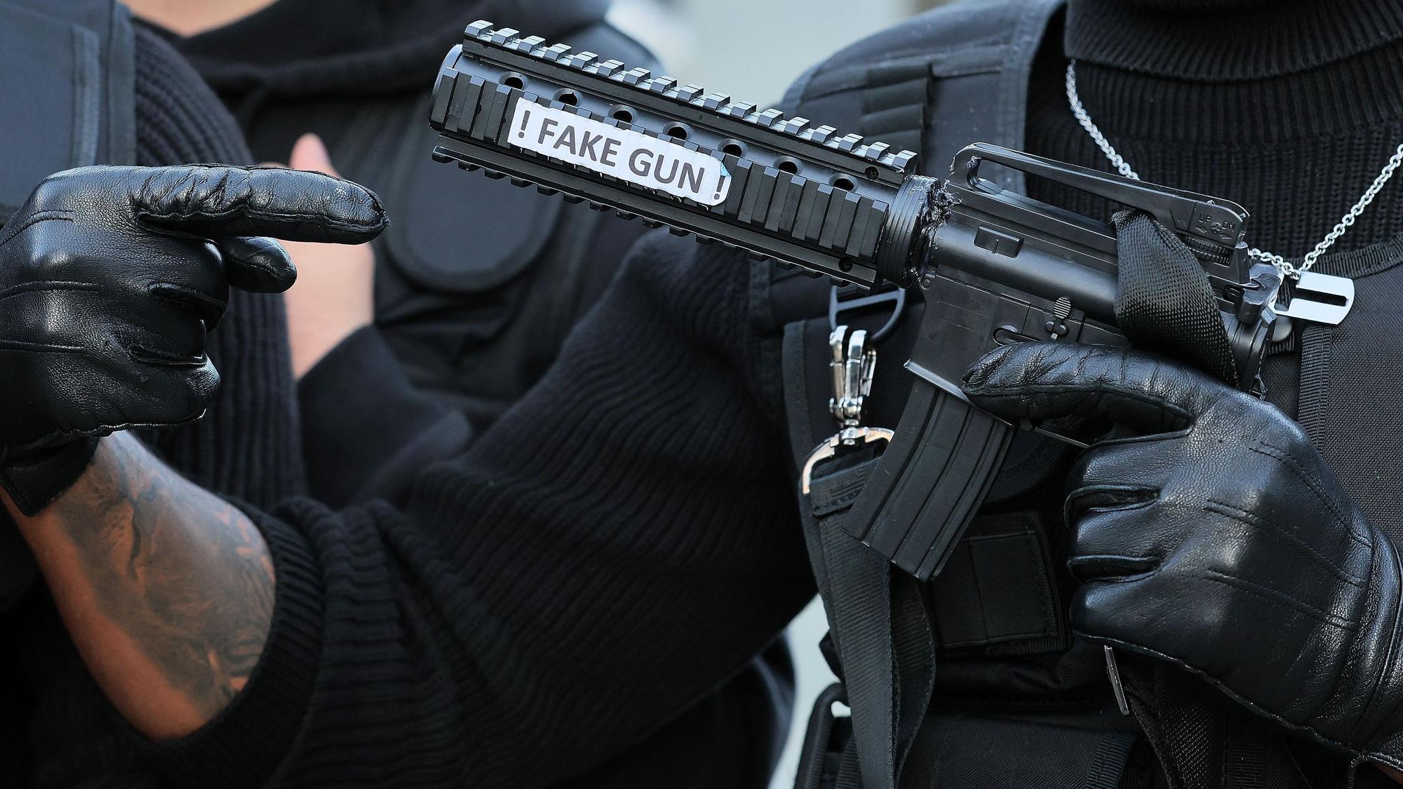 Ein als Swat-Polizist verkleideter Karnevalist hält eine Pistolenattrappe mit der Aufschrift „Fake Gun“ in der Hand.