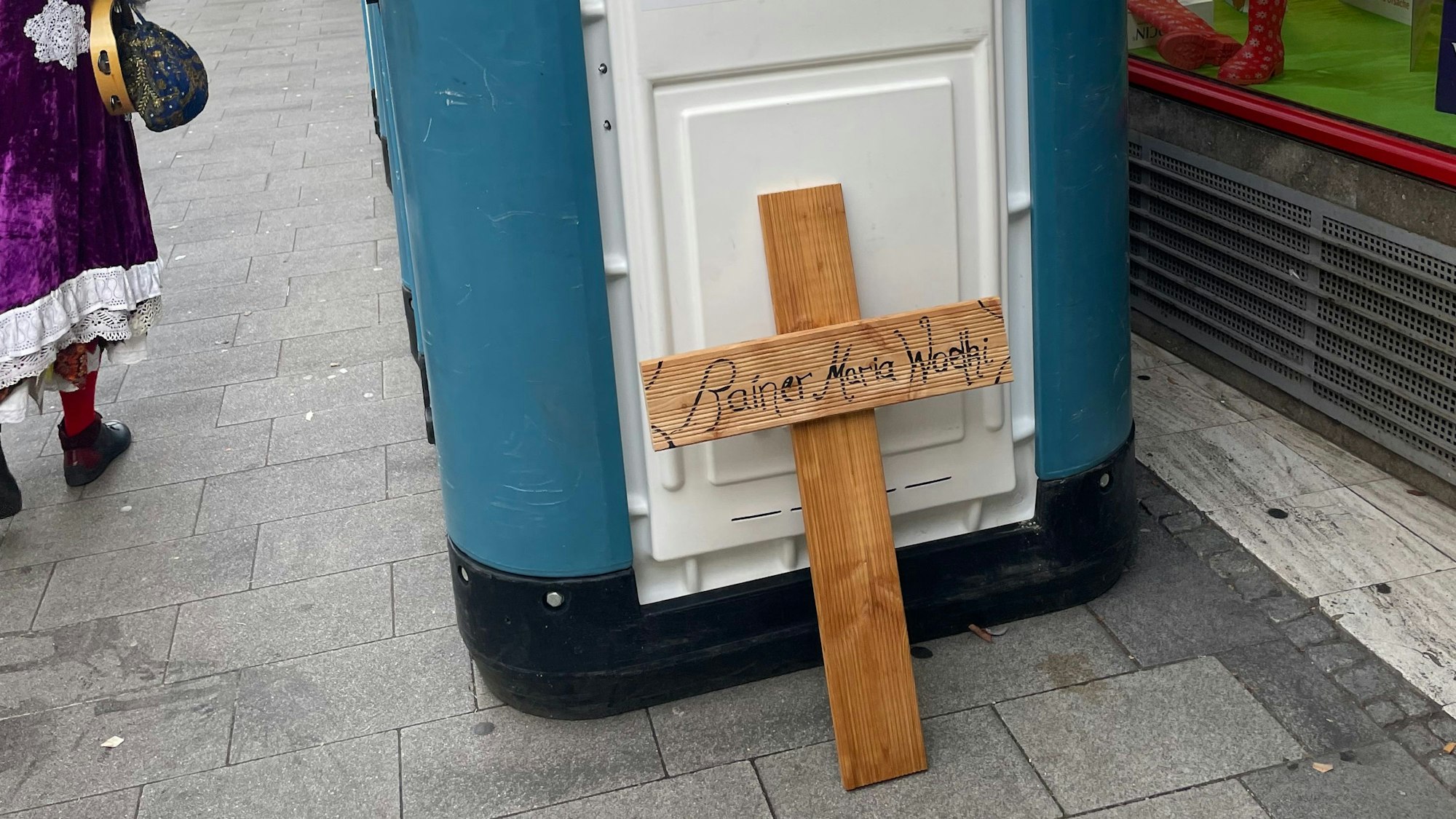 Ein Holzkreuz mit der Aufschrift „Rainer Maria Woelki“ wurde an ein Dixiklo gelehnt.