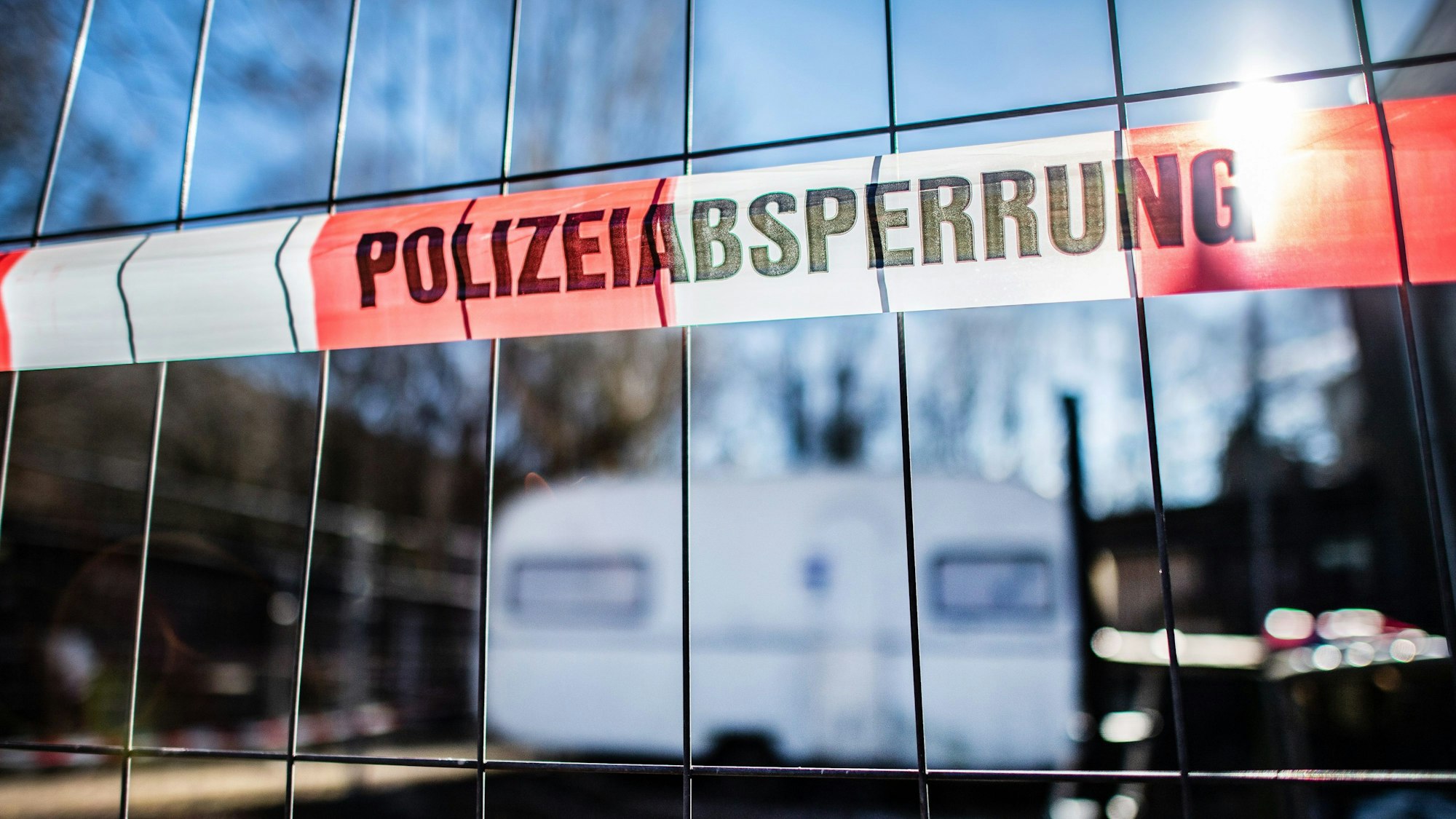 Absperrband der Polizei hängt an einem Bauzaun. Dort hinter befindet sich ein Wohnwagen.