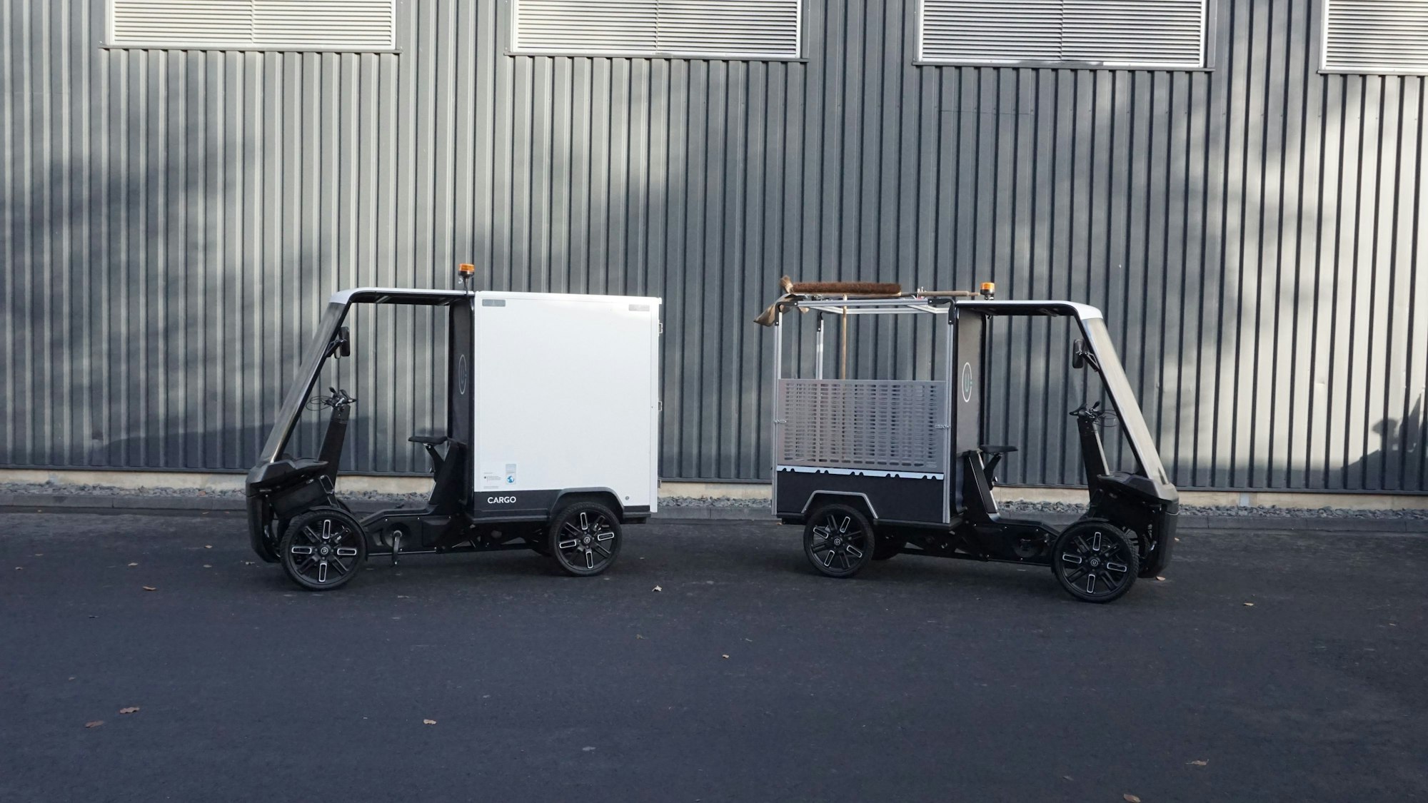 Vor einer Wand stehen die beiden vierrädrigen Kabinenfahrzeuge.