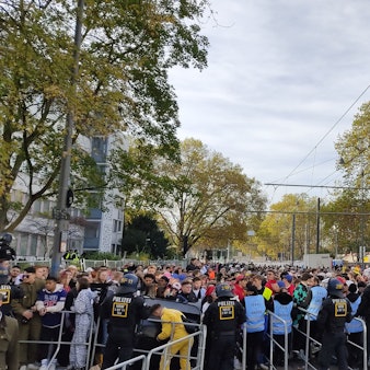 Hunderte junge Leute drängen auf die Absperrungen an der Zülpicher Straße. Die Sicherheitskräfte in blauen Westen haben große Mühe, die Menschen zurückzuhalten.