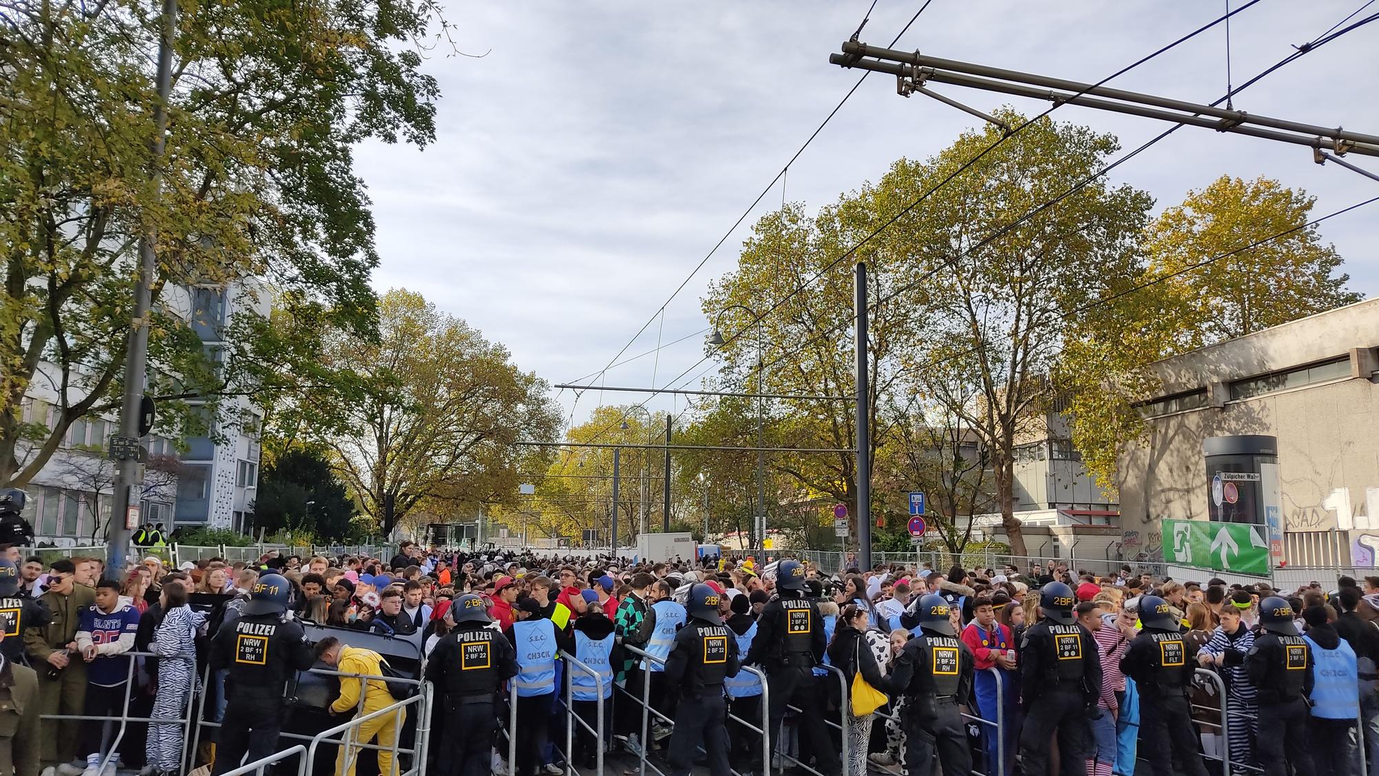 Hunderte junge Leute drängen auf die Absperrungen an der Zülpicher Straße. Die Sicherheitskräfte in blauen Westen haben große Mühe, die Menschen zurückzuhalten.