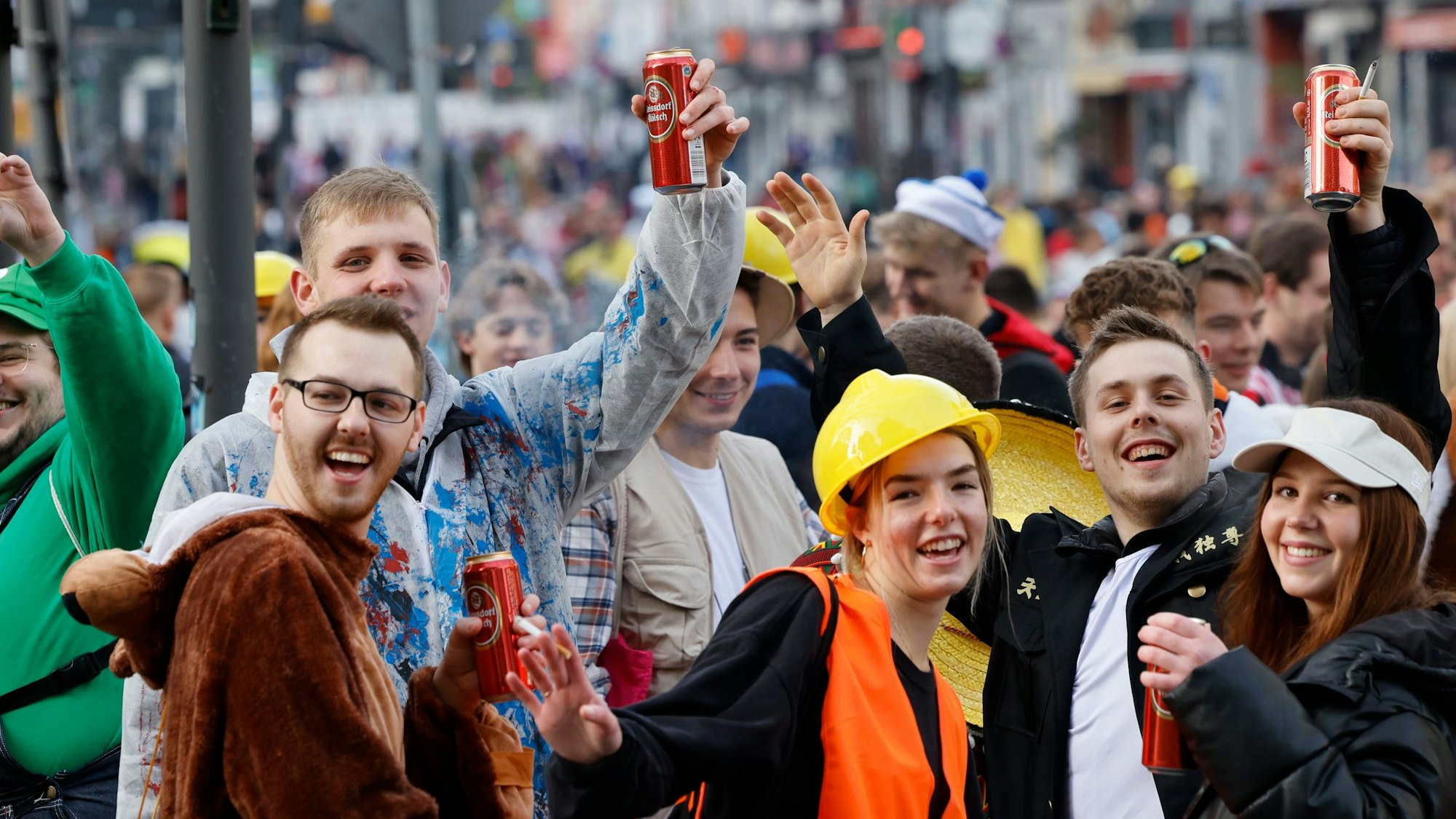 Mehrere verkleidete Menschen lächeln in die Kamera, einige halten Kölsch-Dosen hoch.