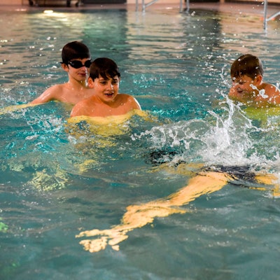 Vier Kinder üben im Wasser mit ihrem Schwimmlehrer.