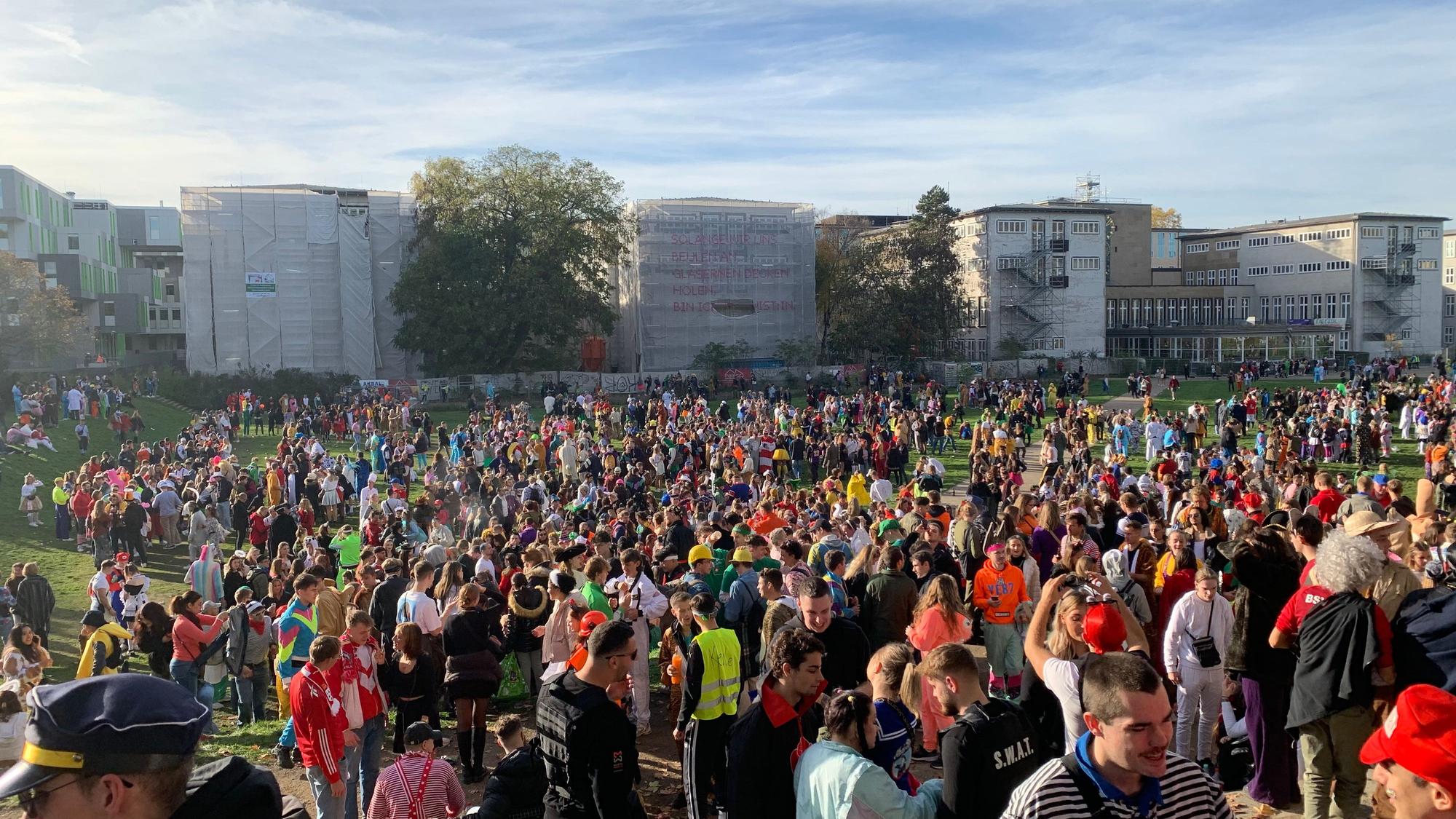 Hunderte junge Leute feiern bunt kostümiert am Elften Elften 2022 auf der Uniwiese. Nach den Feierlichkeiten war die Wiese stark verschmutzt. Im Hintergrund ist die Universität zu Köln zu sehen.