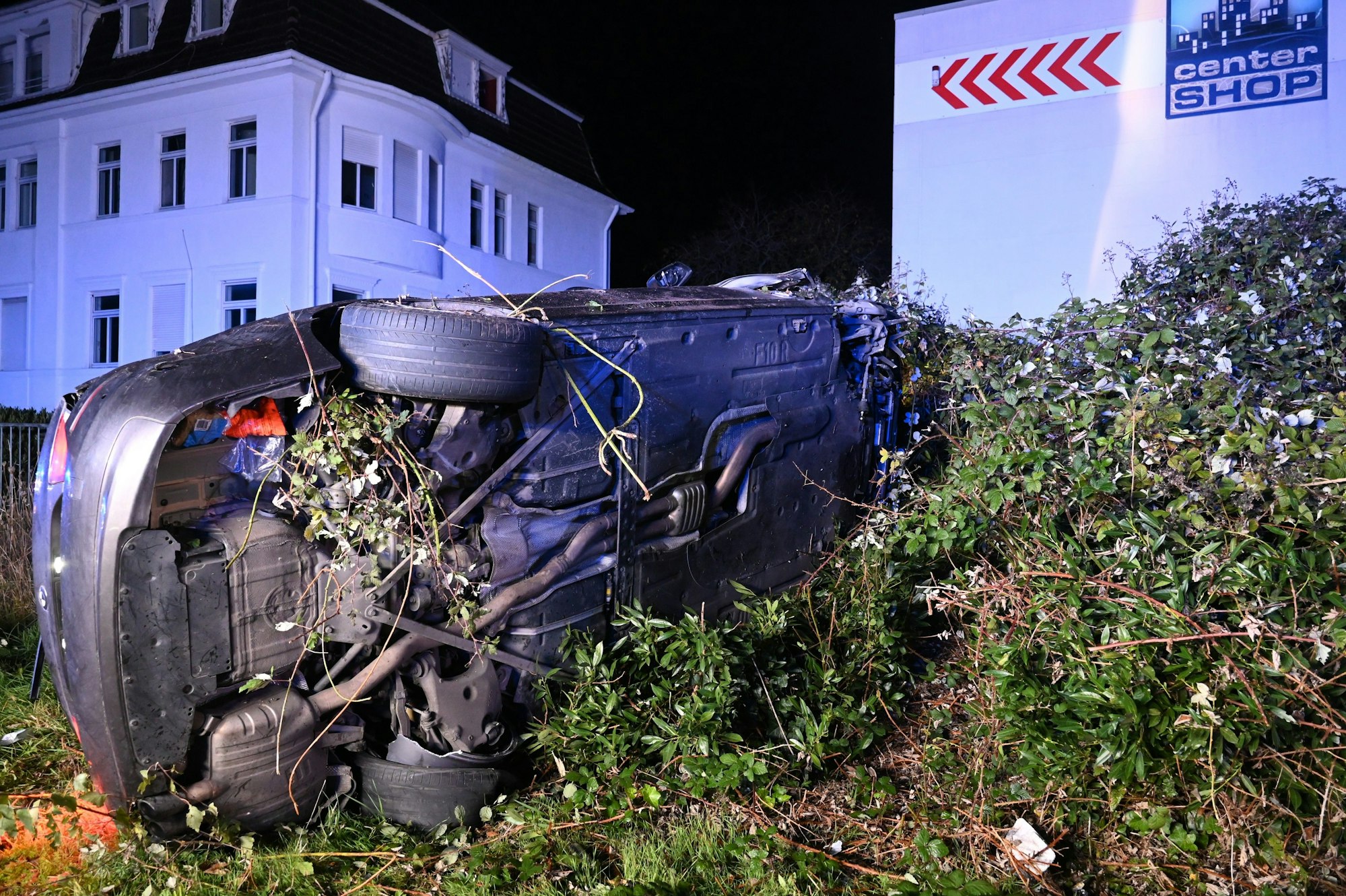 Ein Auto liegt auf der Seite in einem Gebüsch neben der Straße.