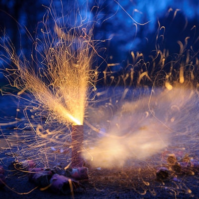 Zu sehen ist ein Böller, der auf dem Boden steht und Funken sprüht. Die Umgebung ist dunkel.