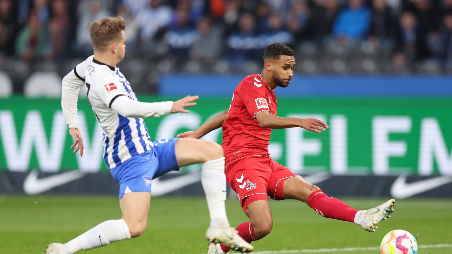 Linton Maina vom 1. FC Köln schießt den Ball. Maximilian Mittelstadt versucht den Ball abzuschirmen.