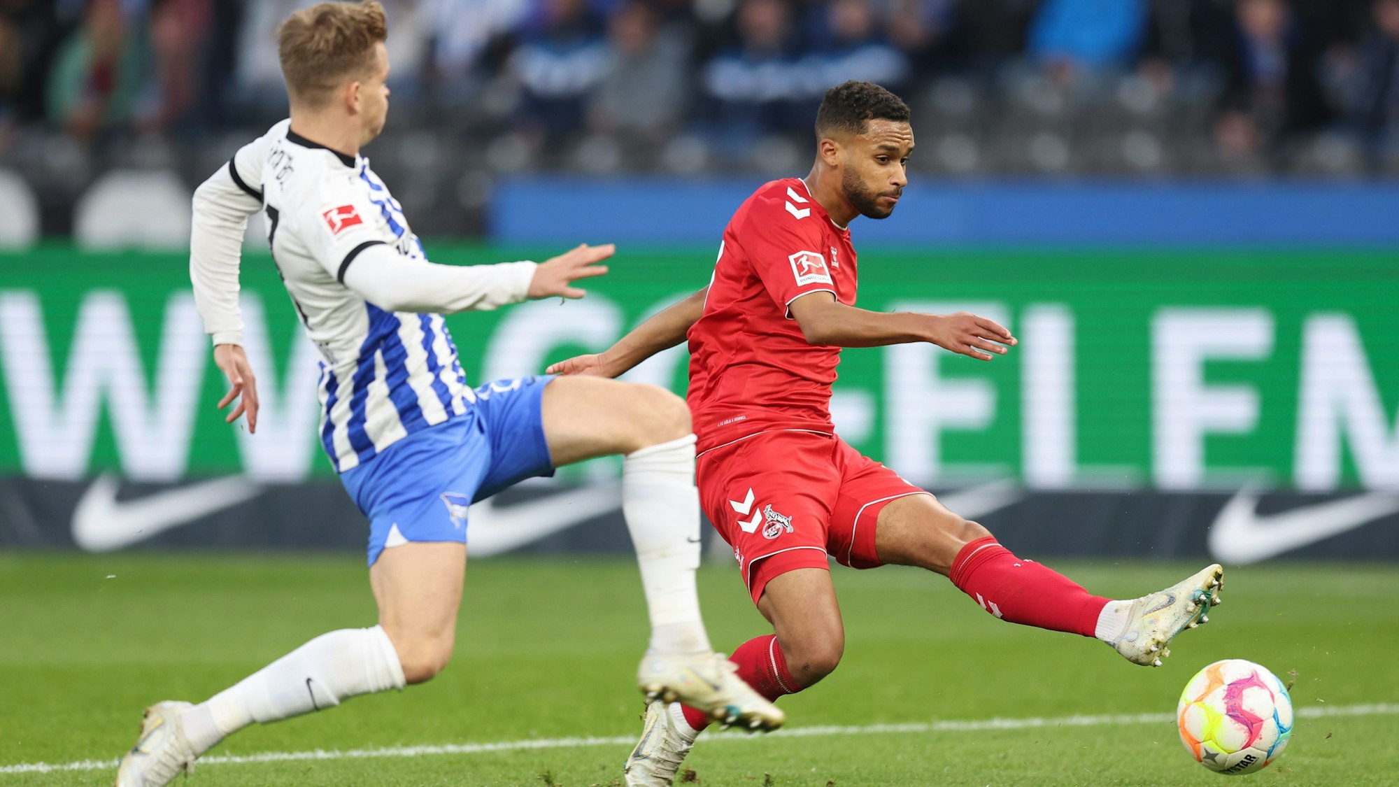 Linton Maina vom 1. FC Köln schießt den Ball. Maximilian Mittelstadt versucht den Ball abzuschirmen.