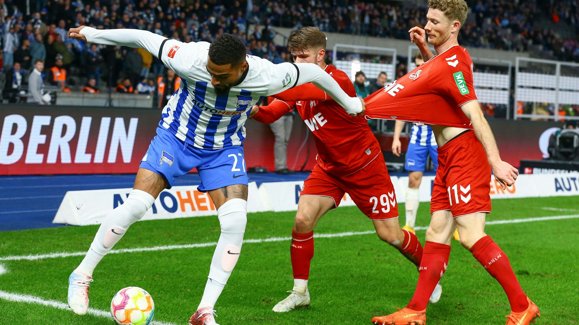 Boateng ist im Ballbesitz, Kainz neben ihm, Thielmann hinter ihm. Thielmann schubst Boateng, dieser hält sich am Shirt von Kainz fest. Sie befinden sich am Spielfeldrand, im Hintergrund sieht man die Zuschauertribünen.