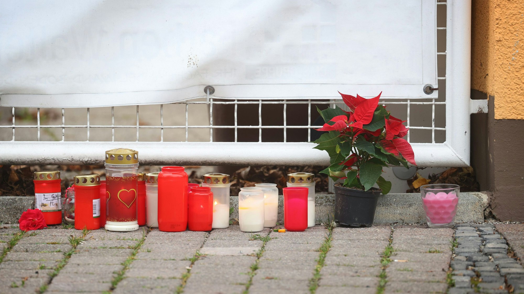 Kerzen und Blumen stehen vor einem Haus in Weilheim, wo sich eine Bluttat mit vier Toten ereignet hat.
