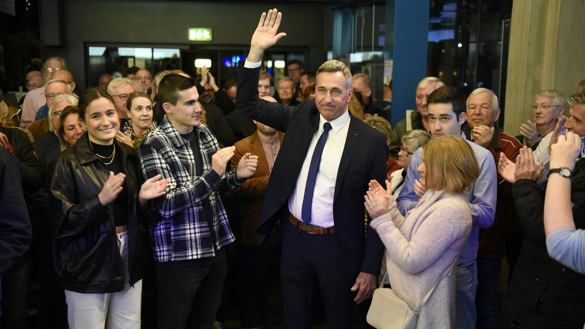 Ralph Manzke, neuer Bürgermeister in Wesseling, steht vor zahlreichen Menschen und feiert seinen Wahlsieg. Er trägt einen Anzug mit blauer Krawatte.