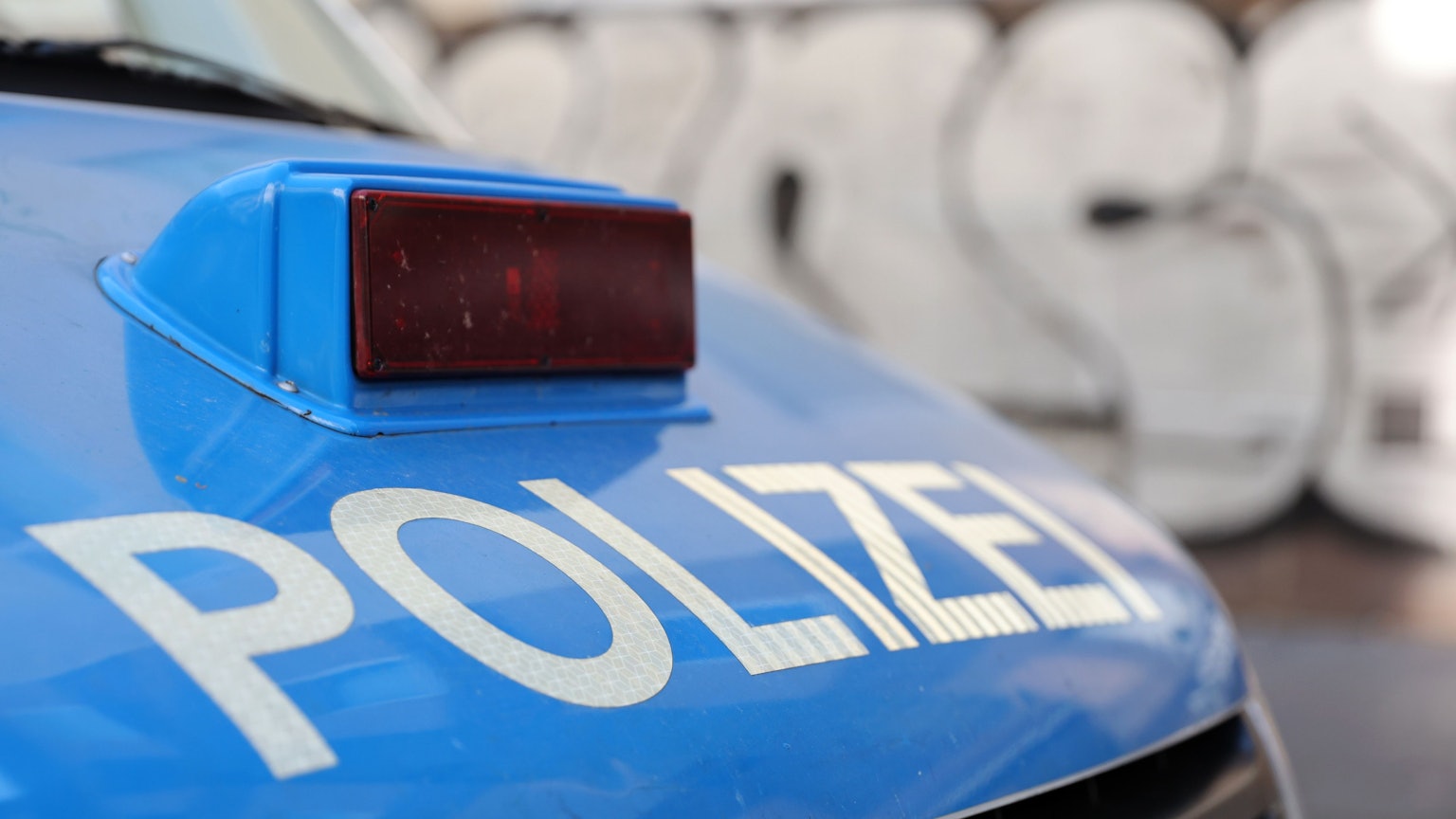 Die Motorhaube eines Polizeiautos mit rot verblendeter Sirene und der weißen Aufschrift „Polizei“.