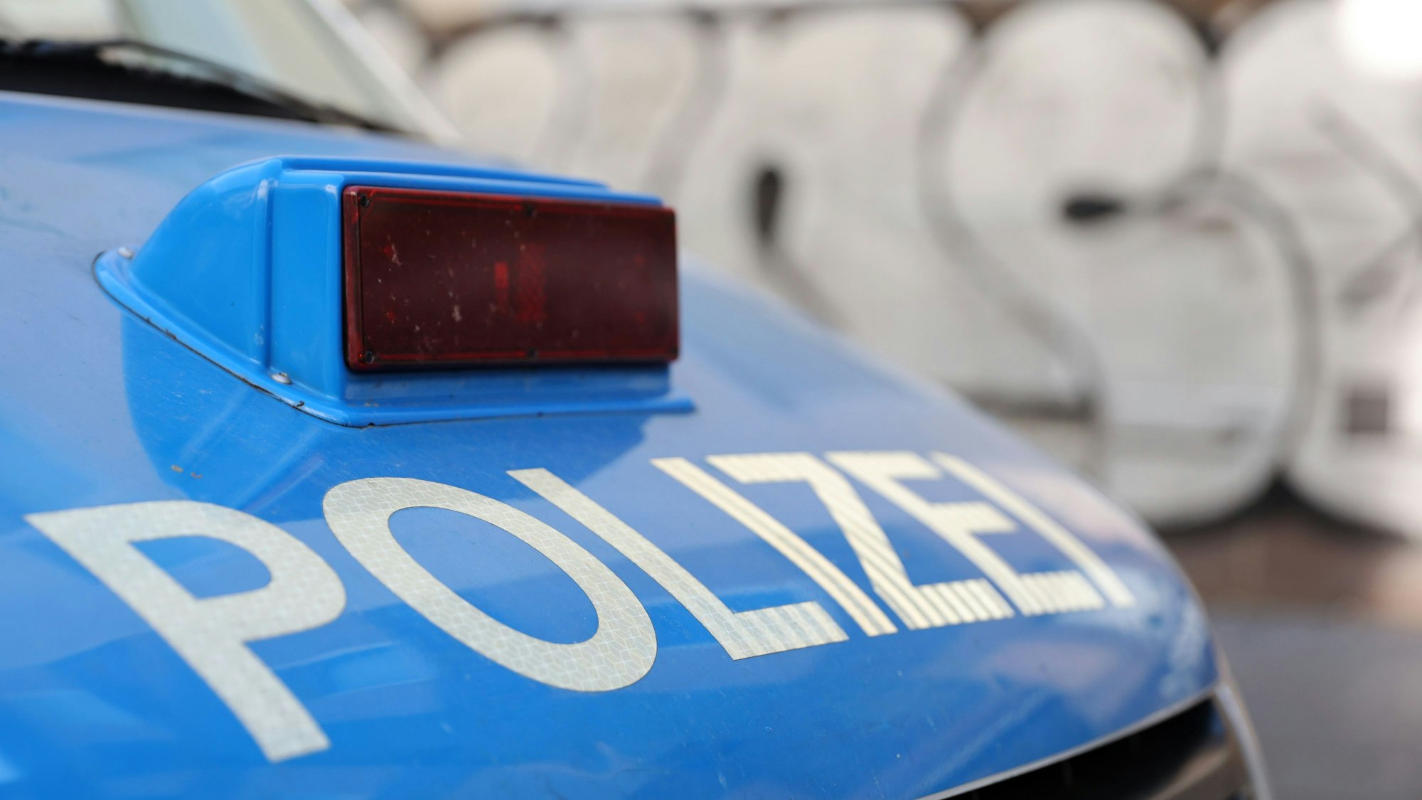 Ein Polizeiauto steht auf einer Straße. Im Hintergrund ist unscharf eine mit Graffiti besprühte Mauer zu sehen.
