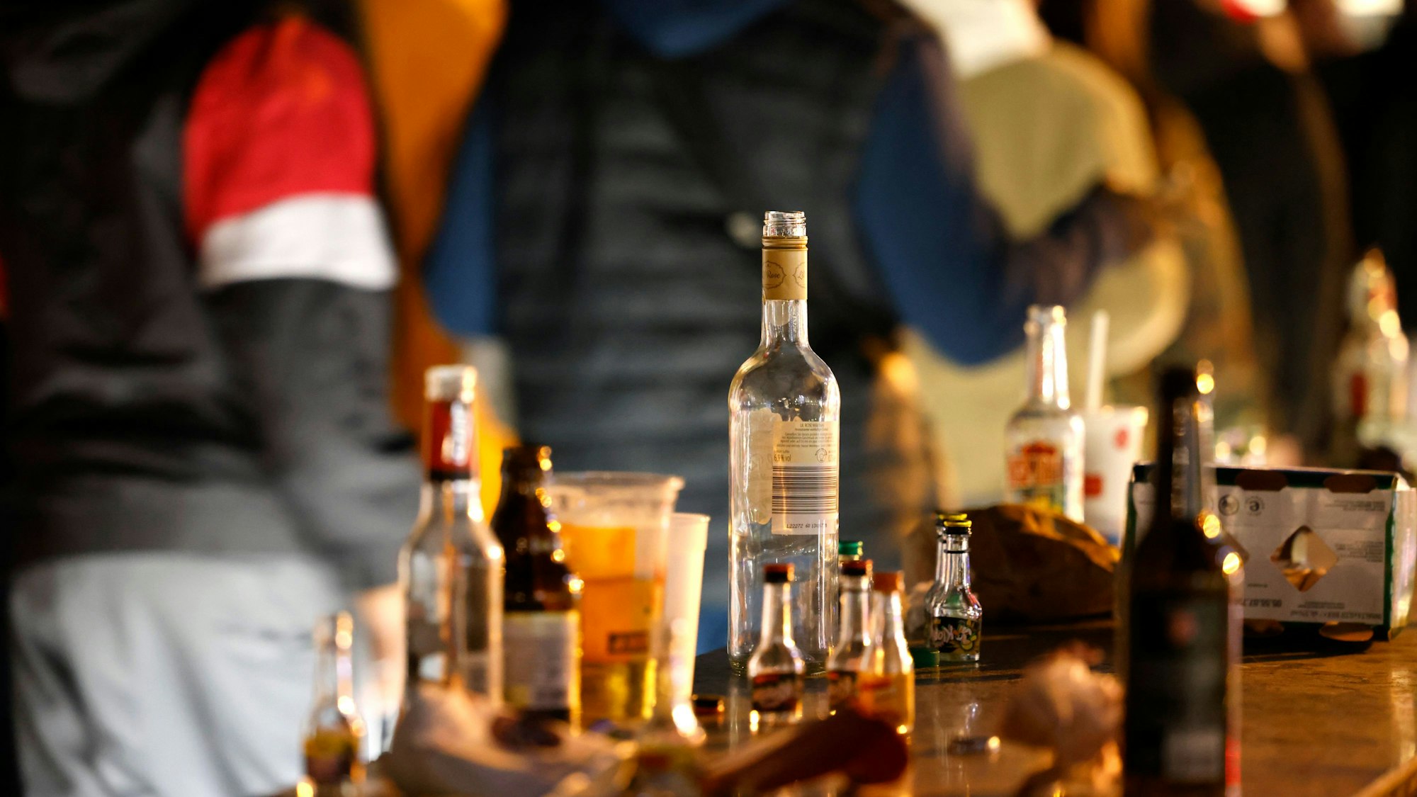 Leere Flaschen stehen auf einem Tresen. Dahinter sieht man einige Personen weggehen.
