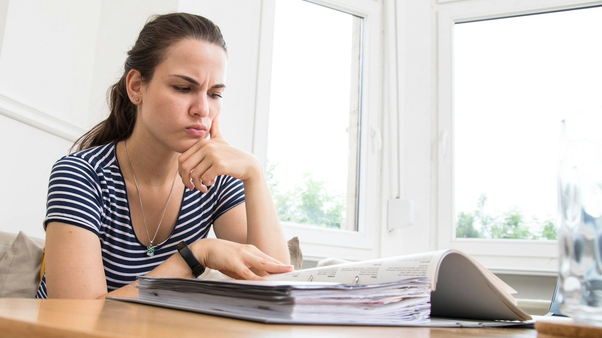 Eine Frau blickt kritisch auf einen Aktenordner mit Rechnungen.