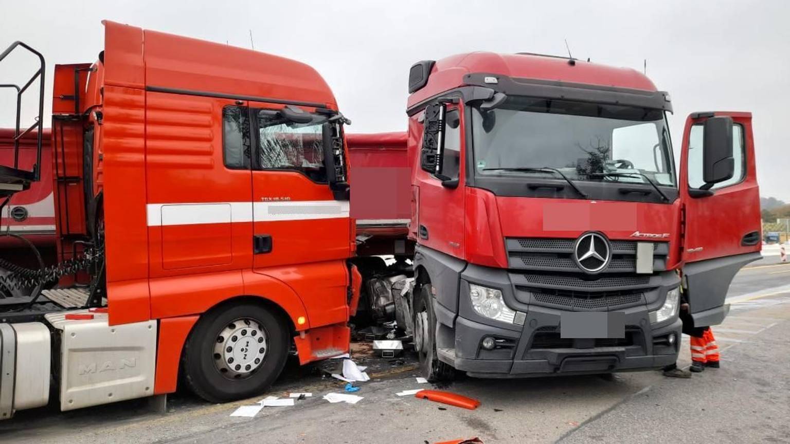 Zwei rote Lkw-Fahrerkabinen stehen beschädigt auf der Autobahn. Auf dem Boden liegen Papiere und abgeplatztes Plastik verteilt.