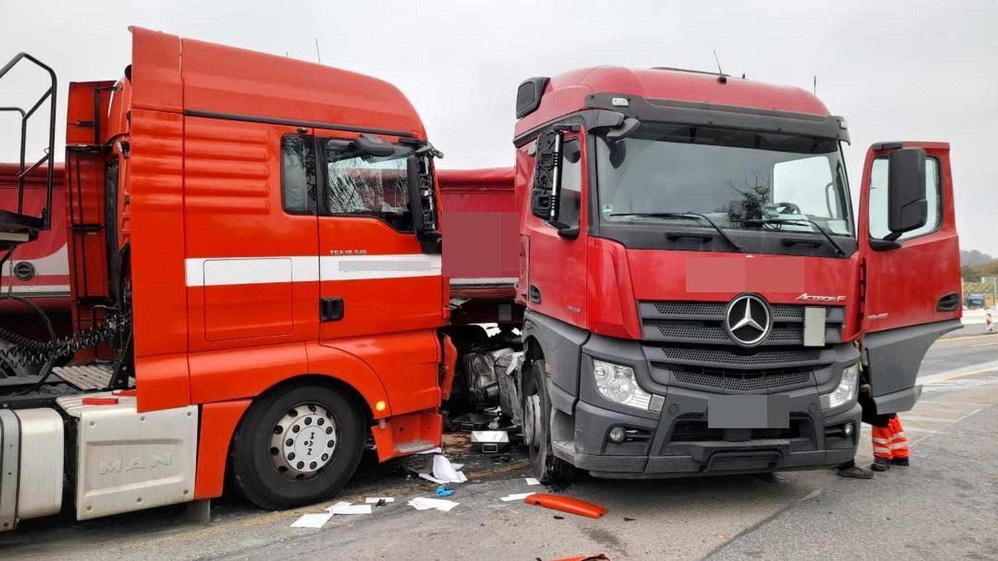 Zwei rote Lkw-Fahrerkabinen stehen beschädigt auf der Autobahn. Auf dem Boden liegen Papiere und abgeplatztes Plastik verteilt.