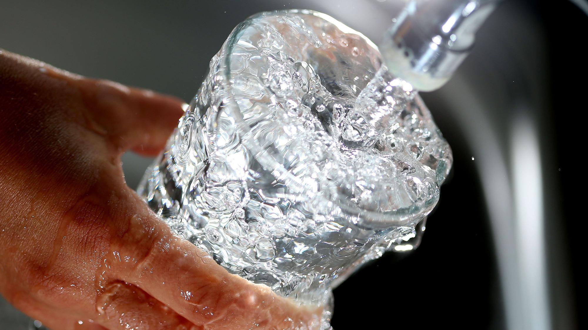 Ein Glas wird an einem Wasserhahn mit Wasser gefüllt.