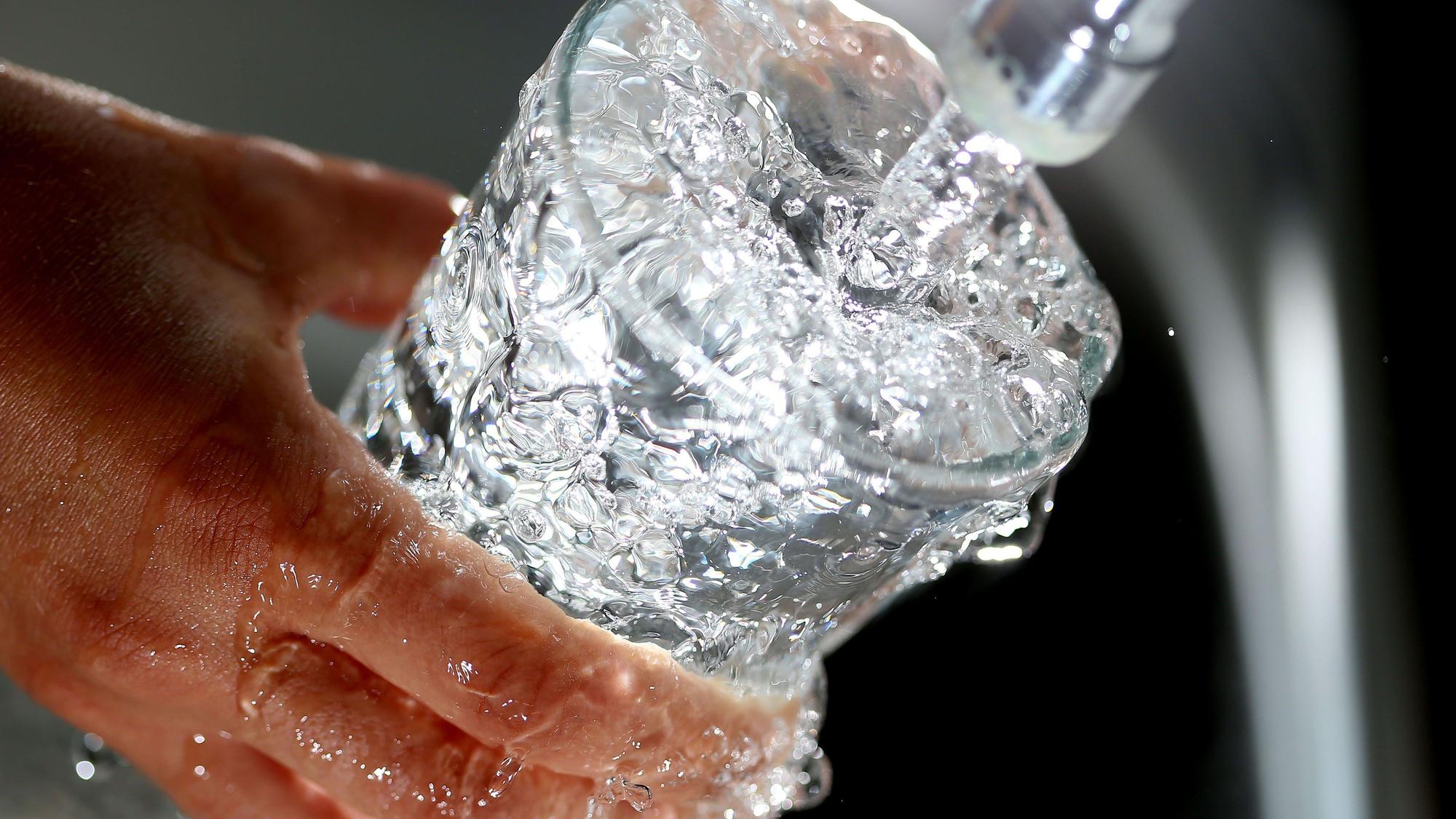 Eine Hand hält ein Glas, in das Trinkwasser aus einem Wasserhahn läuft.