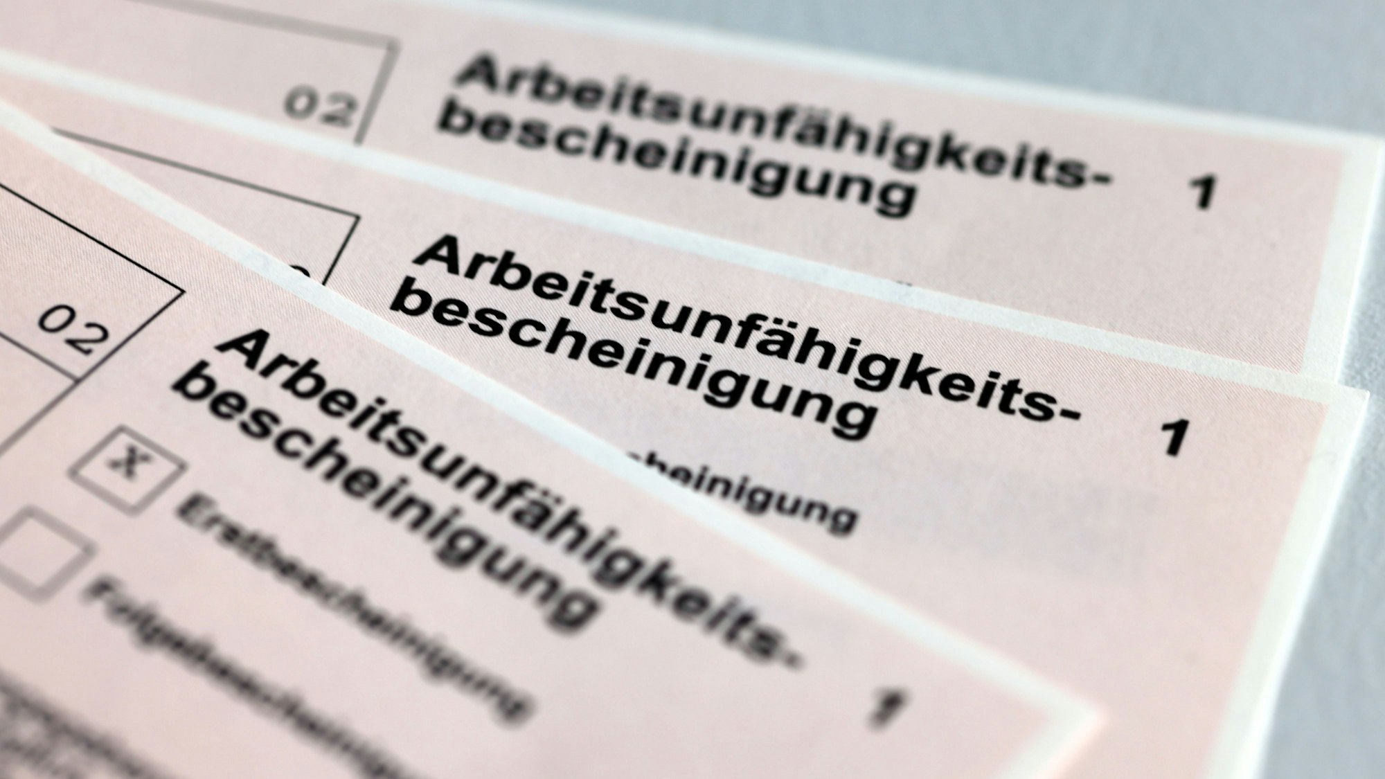 Drei Arbeitsunfähigkeitsbescheinigungen für Arbeitnehmer liegen aufgefächert übereinander.