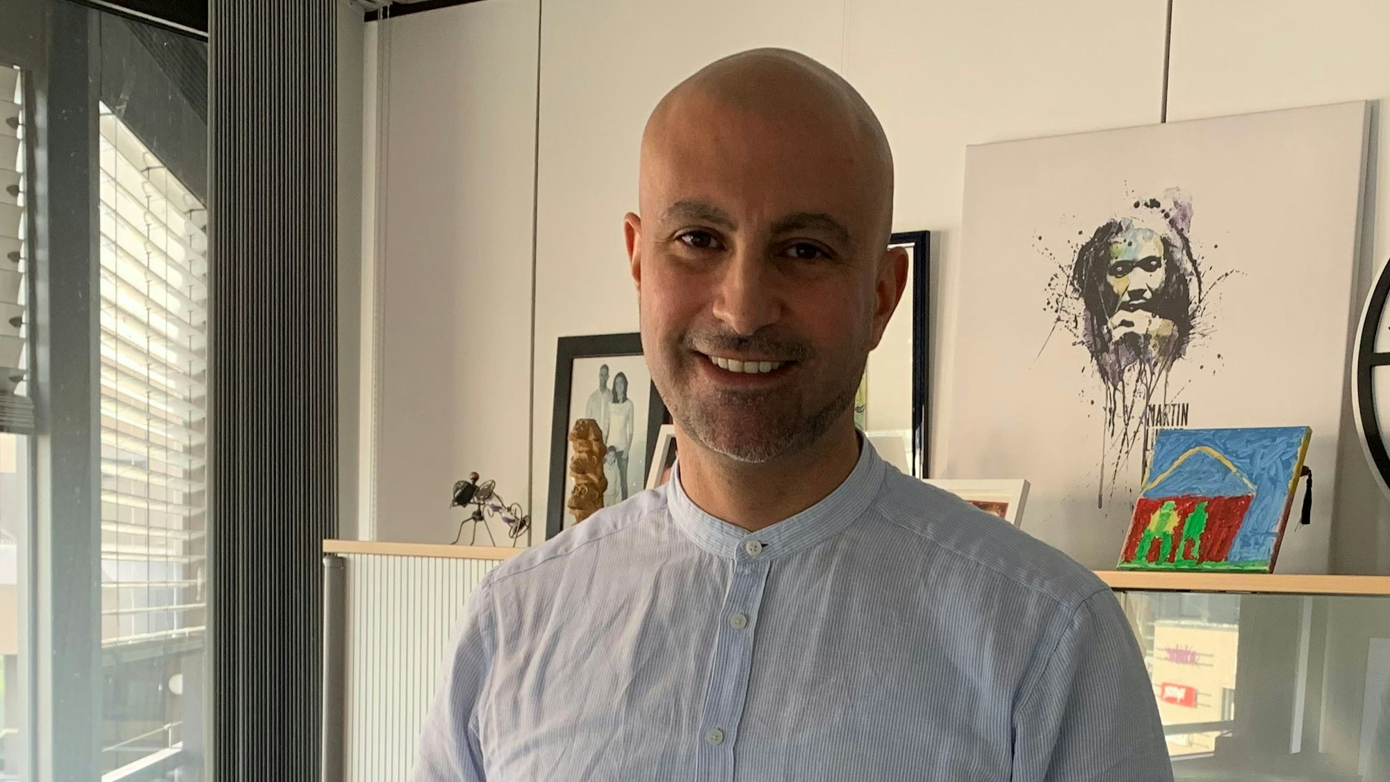 Der SPD-Politiker Ali Dogan trägt ein blaues Hemd und steht in seinem Büro im Rathaus von Sankt Augustin.