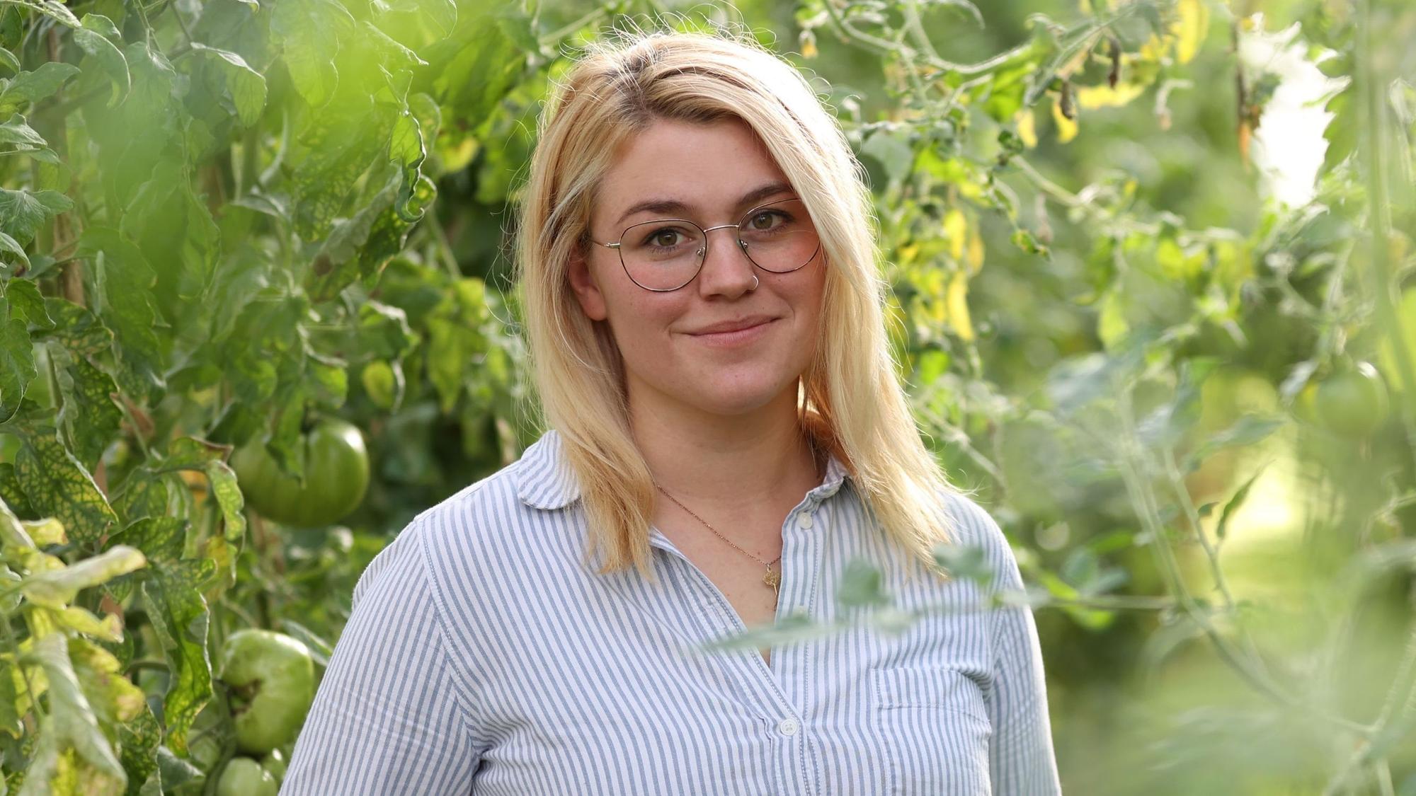 Caroline Uhl steht inmitten grüner Pflanzen.