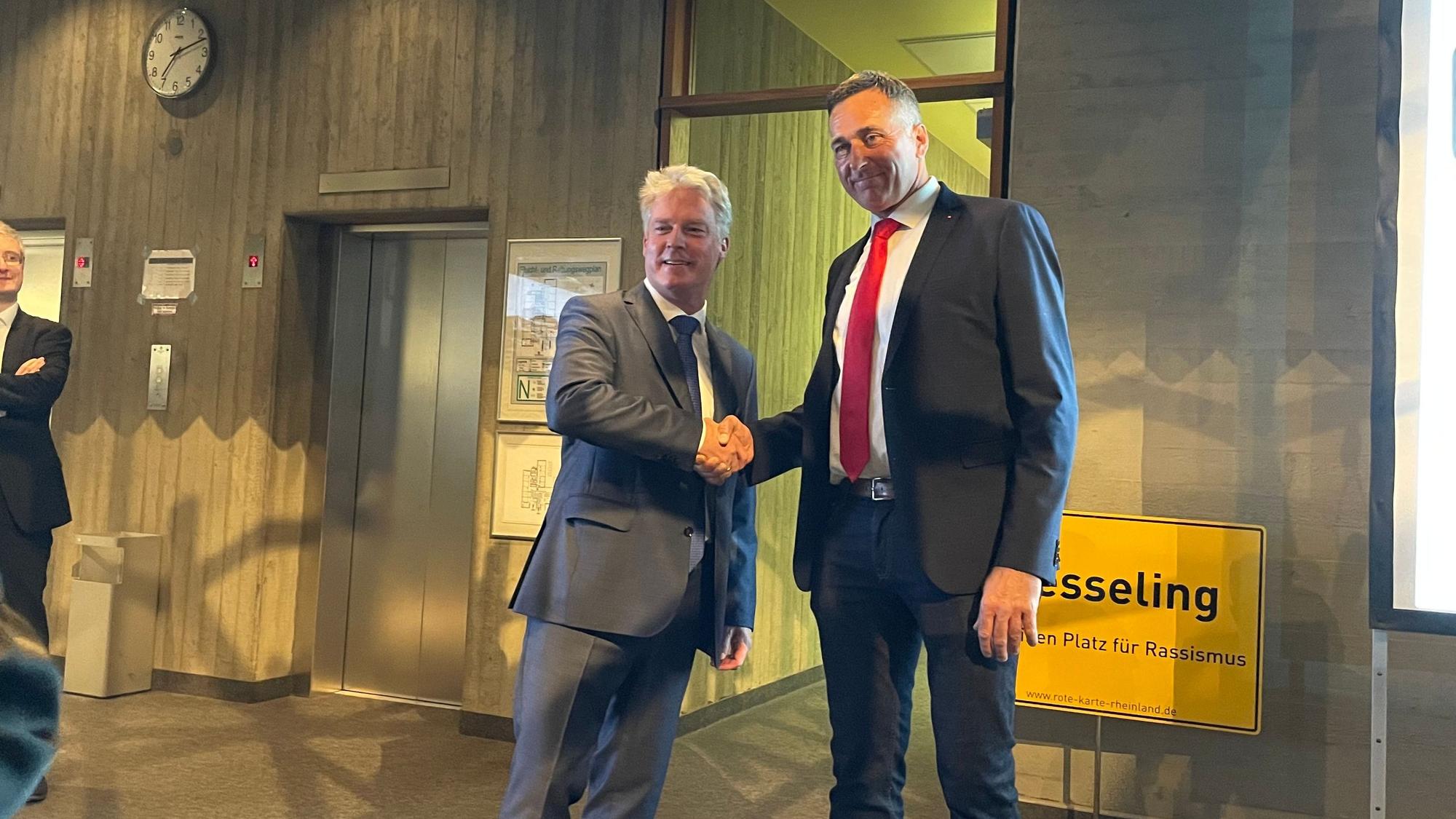 Olaf Krah (links) schüttelt seinem Kontrahenten Ralph Manzke die Hand. im Hintergrund ist ein Schild mit der Aufschrift „Wesseling“ zu sehen.