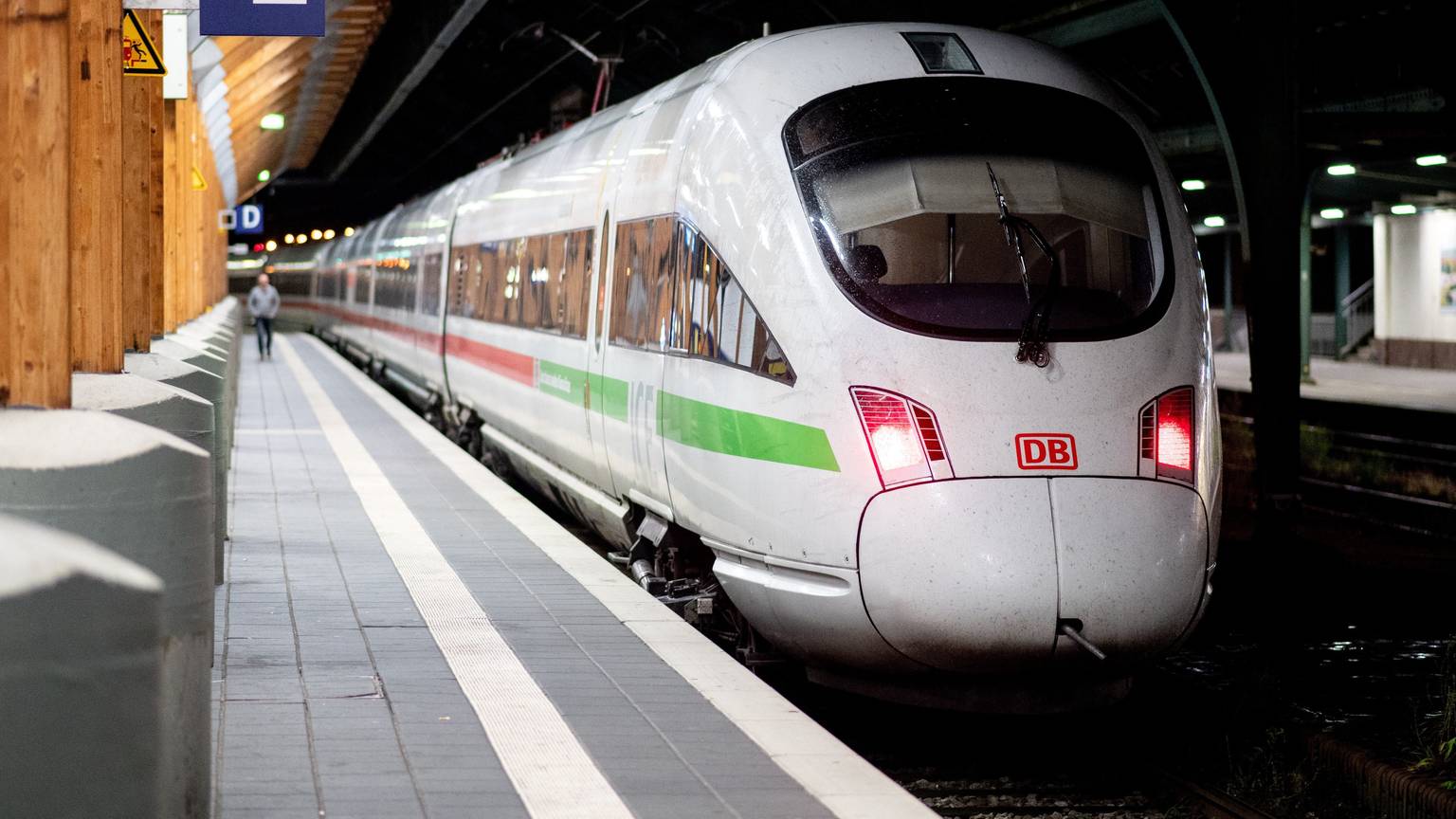 Ein ICE steht an einem Bahnhof. Auf dem Bahnsteig läuft im Hintergrund eine Person. Es ist dunkel.