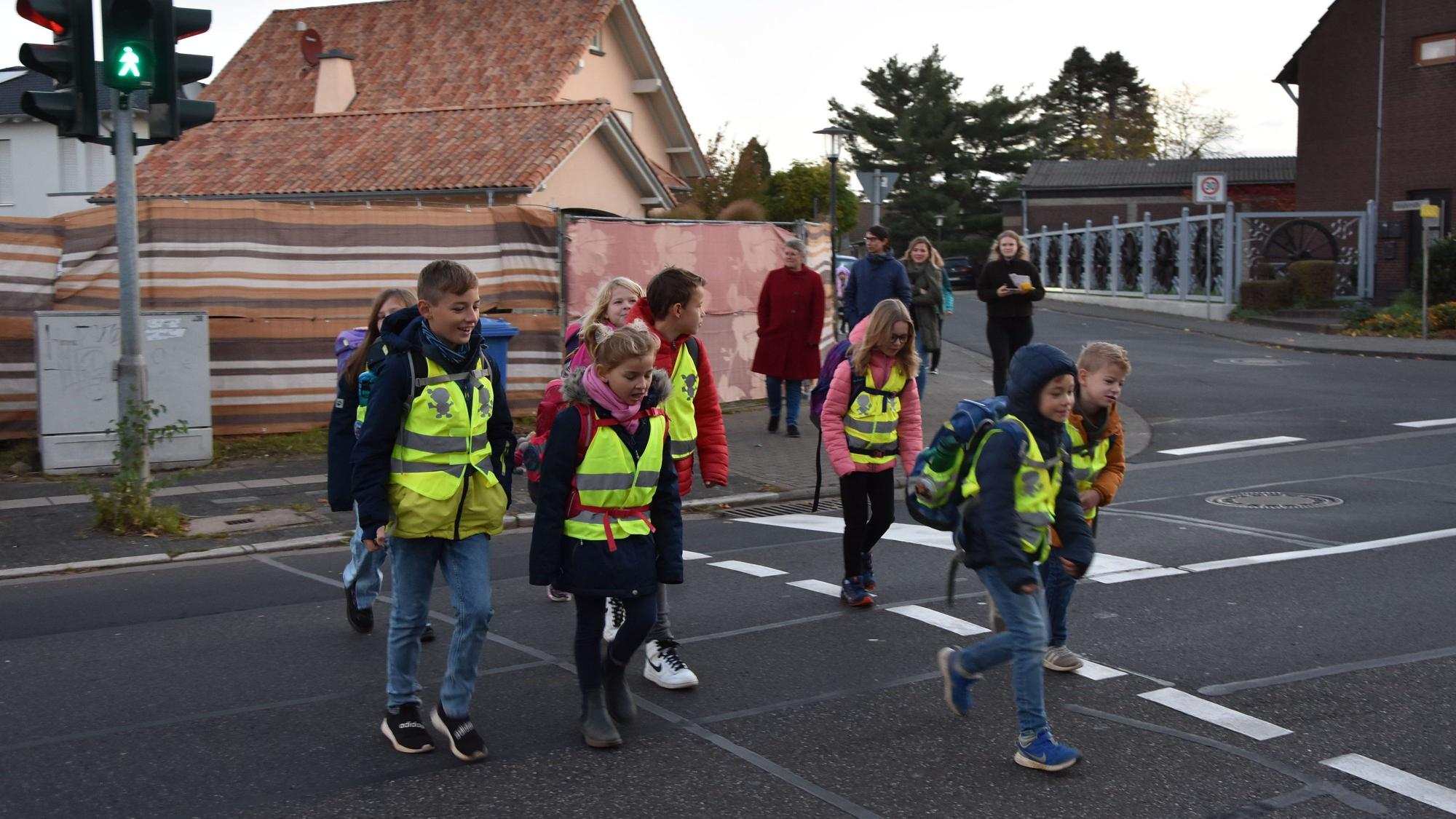 Schulkinder in gelben Warnwesten überqueren die Straße an einer Ampel.