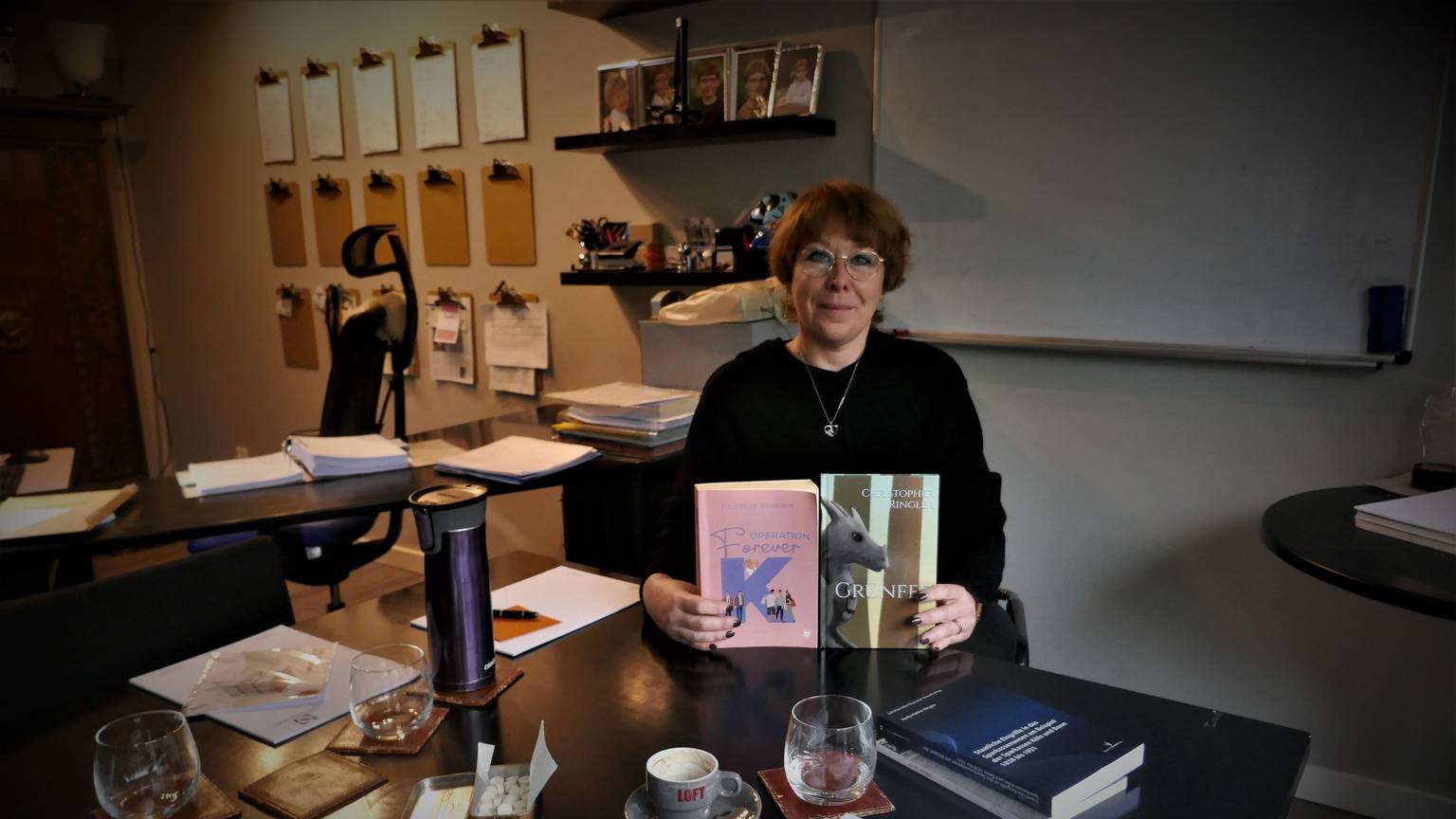 Die Autorin Nadja Kobler-Ringler, alias Georgie Severin, sitzt an einem Schreibtisch und zeigt zwei Bücher, ihr eigenes und das ihres Sohnes Christopher.