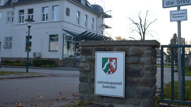 Am Eingang der Justizvollzugsanstalt Euskirchen hängt ein Schild mit dem Wappen des Landes NRW. Im Hintergrund sieht man ein Gebäude.