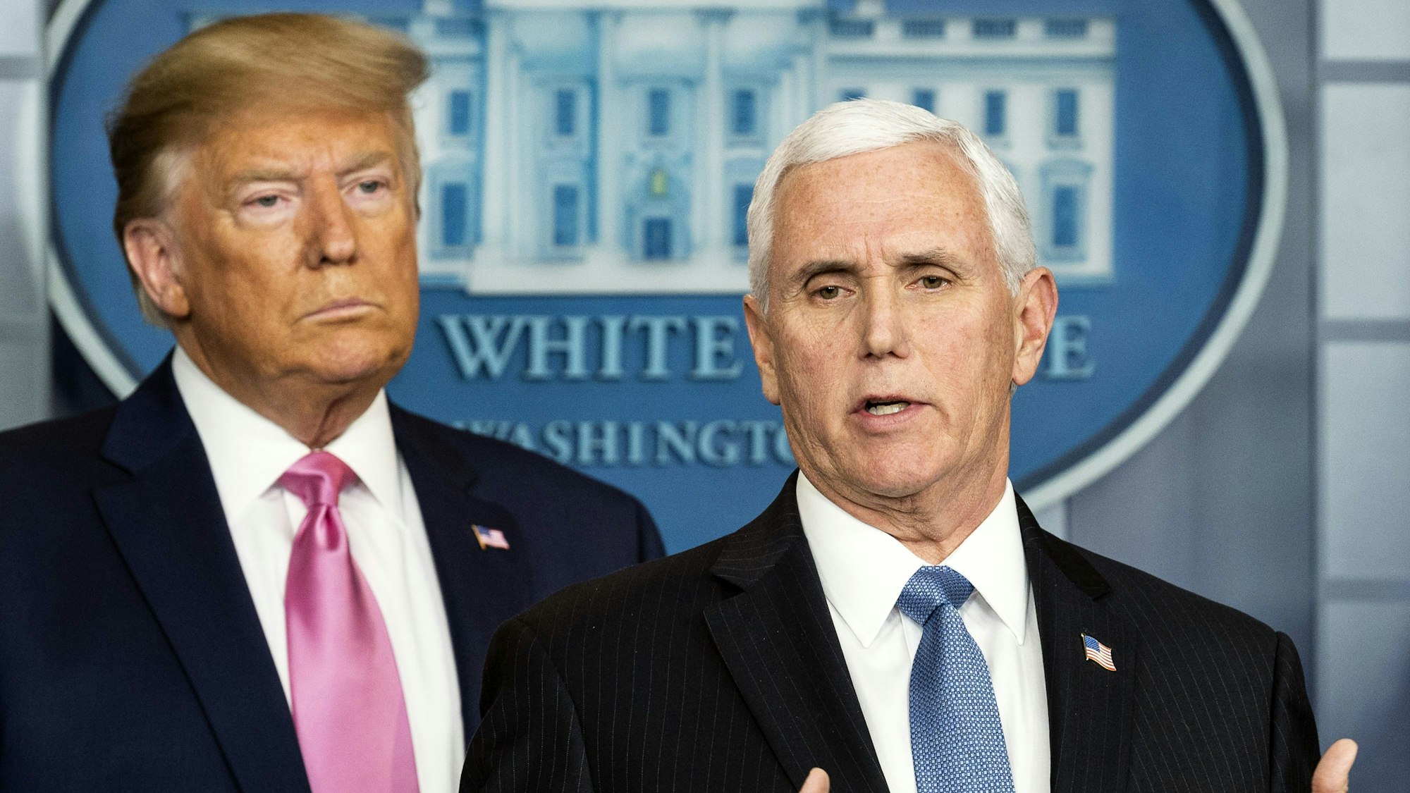 Mike Pence und Donald Trump sprechen auf einer Pressekonferenz im Weißen Haus. Pence steht im Vordergrund und spricht, Trump steht im Hintergrund und guckt mürrisch.