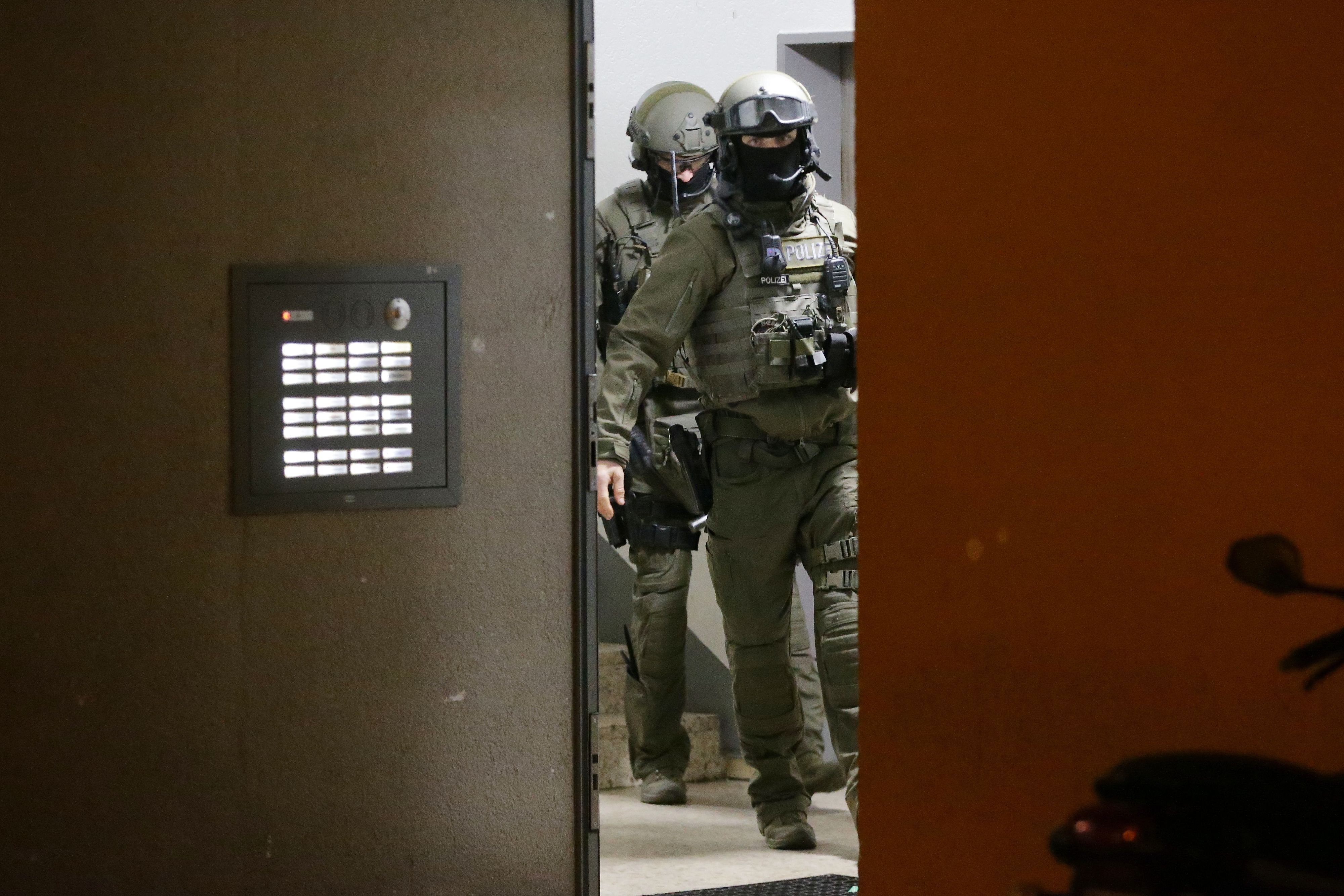 Polizisten vom SEK verlassen ein Mehrfamilienhaus, sie sind schwer gerüstet, die Gesicher sind nicht zu erkennen.