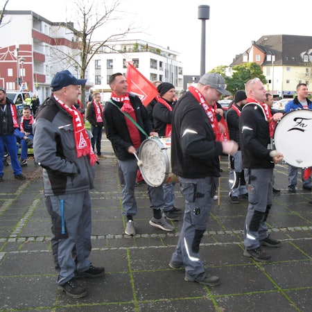 Mehrere Personen stehen auf dem Frouardplatz. Sie haben IG-Metall Schals an und schwenken Fahnen, zwei Männer schlagen auf eine große Trommel.