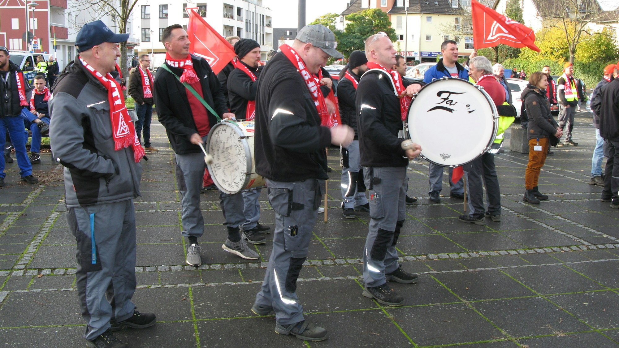 Mehrere Personen stehen auf dem Frouardplatz. Sie haben IG-Metall Schals an und schwenken Fahnen, zwei Männer schlagen auf eine große Trommel.