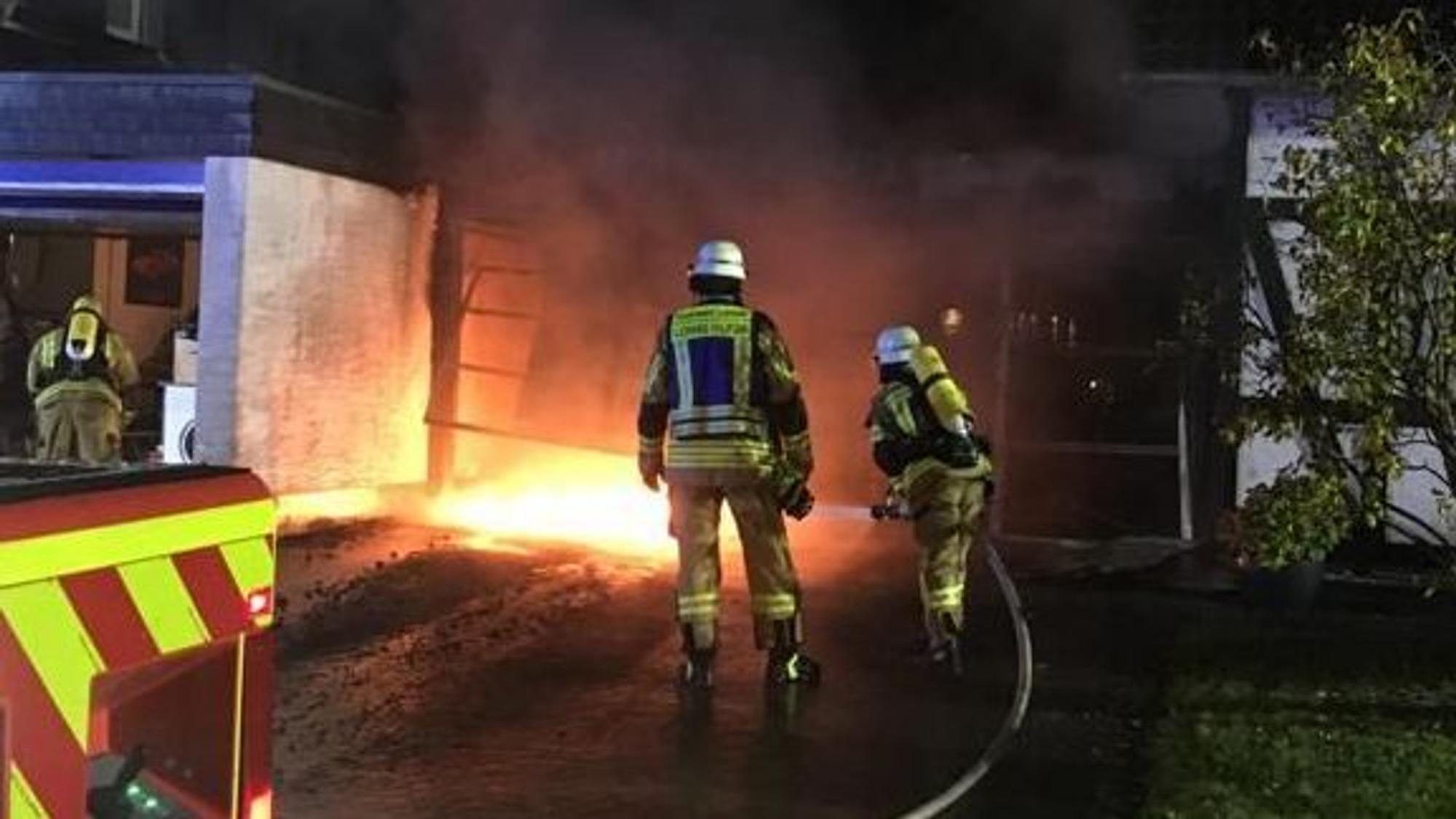 Feuerwehrleute stehen mit einem Feuerwehrschlauch vor einem Feuer.
