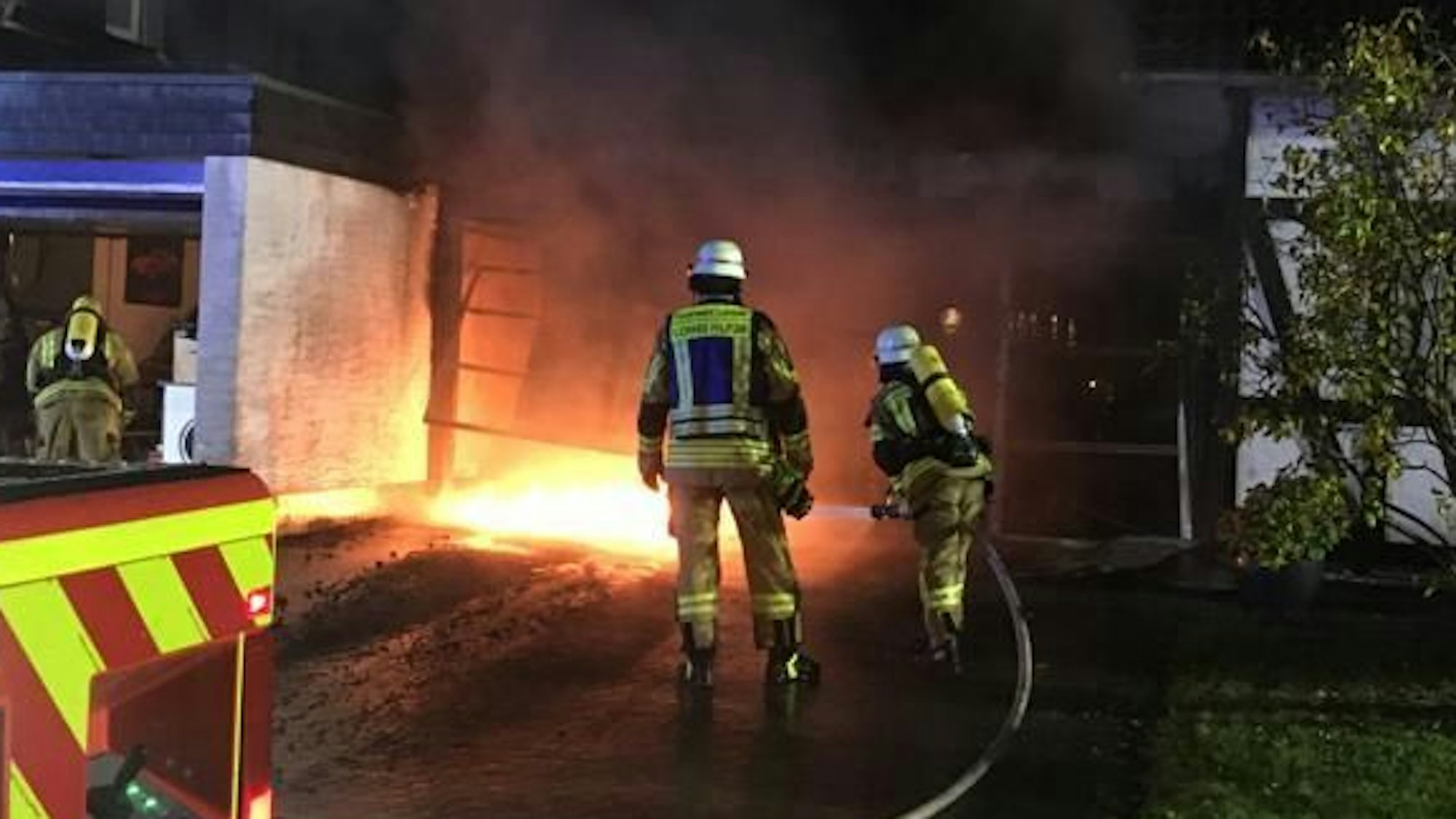 Feuerwehrleute stehen mit einem Feuerwehrschlauch vor einem Feuer.