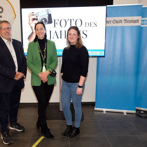Ein Mann und zwei Frauen stehen vor einem Bildschirm mit der Aufschrift „Foto des Jahres“. Daneben stehen Banner vom „Kölner Stadt-Anzeiger“ und „Kölnische Rundschau“.