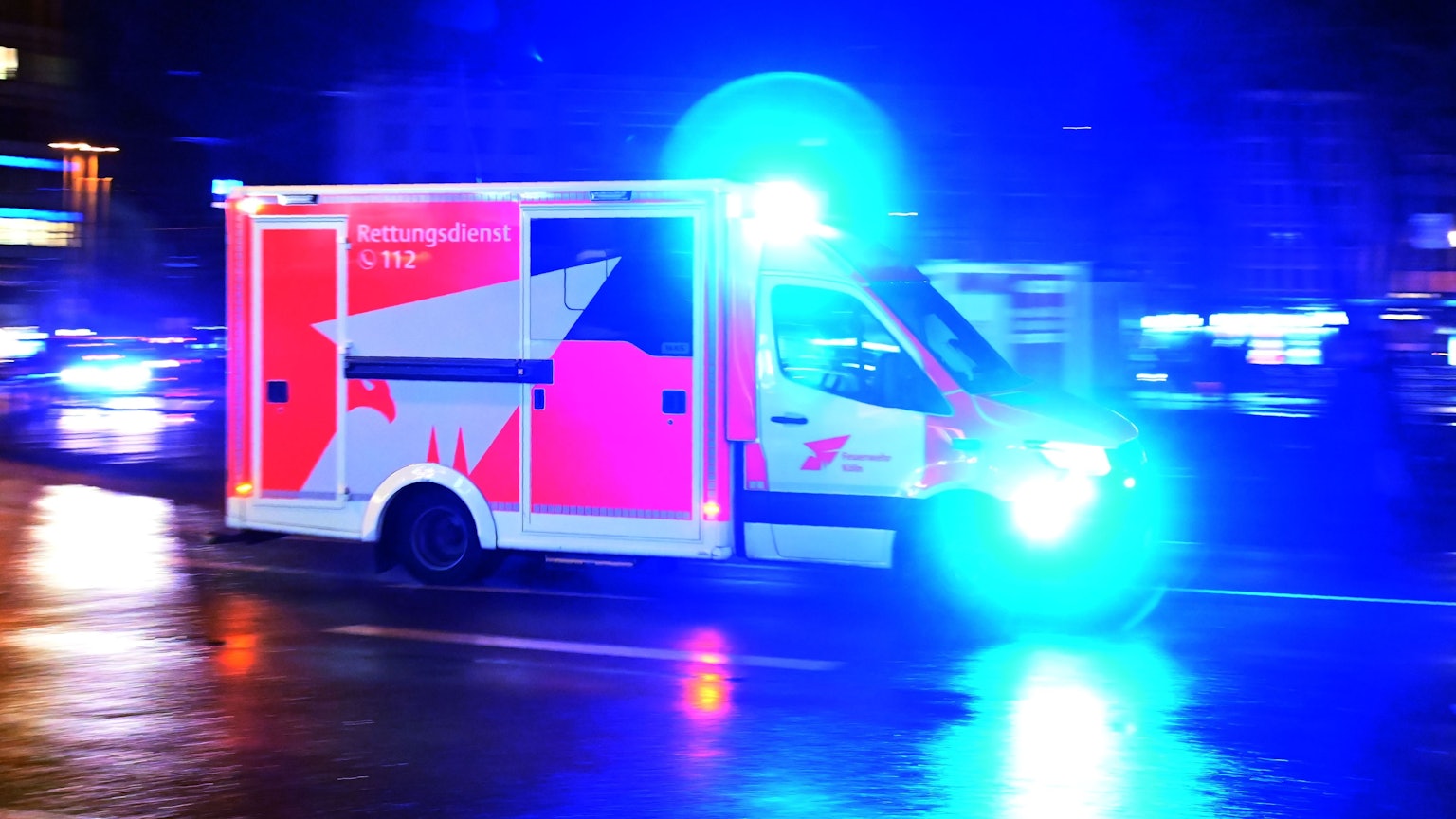 Ein Rettungswagen der Feuerwehr rast nachts über eine Straße.