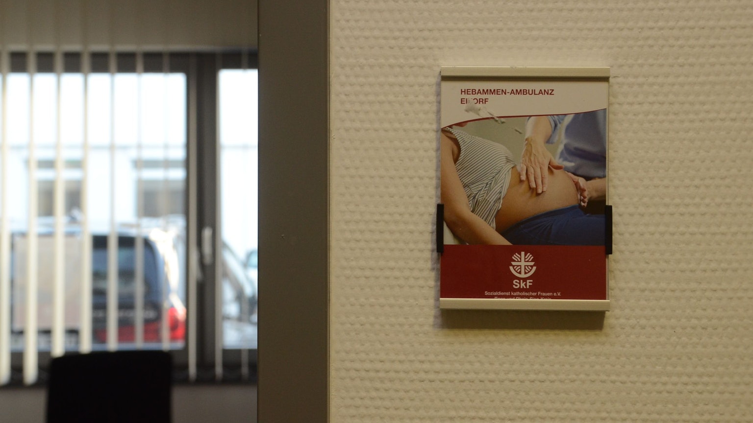 Neben der Tür in ein Beratungszimmer hängt das Plakat mit Werbung für die Hebammenambulanz.