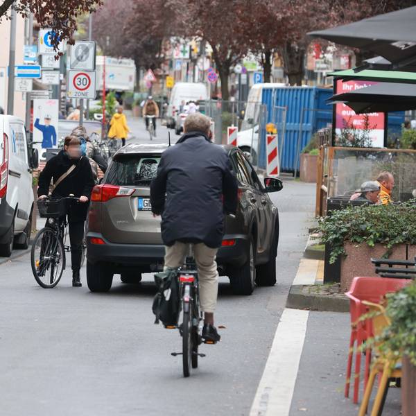 Blick auf die Deutzer Freiheit. Ein Fahrradfahrer und ein Auto stehen in sehr geringem Abstand auf der Straße.