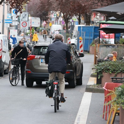 Blick auf die Deutzer Freiheit. Ein Fahrradfahrer und ein Auto stehen in sehr geringem Abstand auf der Straße.