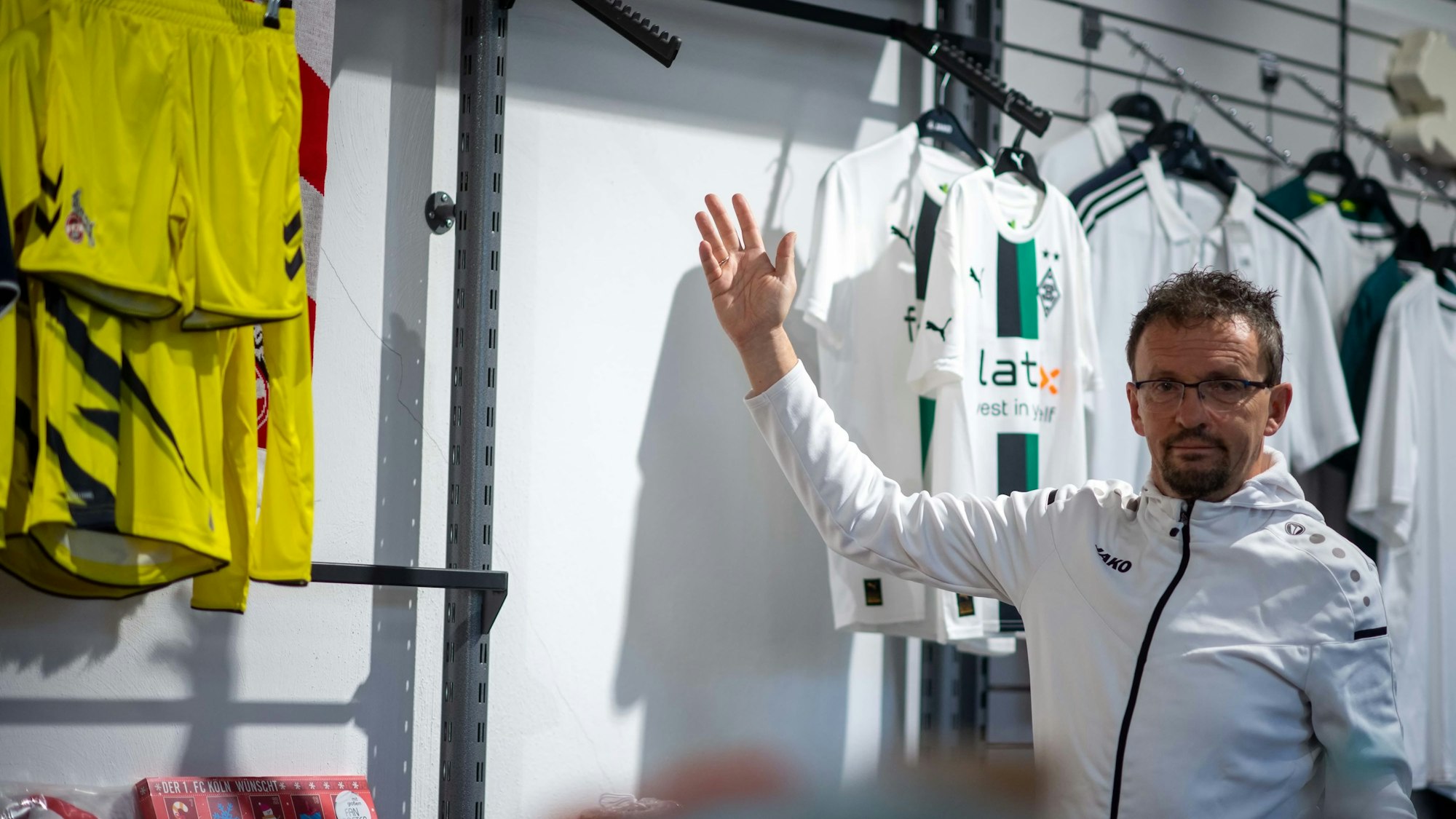Wolfgang Fröhling, Sportgeschäft-Inhaber aus Zülpich, steht vor den Trikots von Borussia Mönchengladbach und Borussia Dortmund, ein Ständer ist leer.