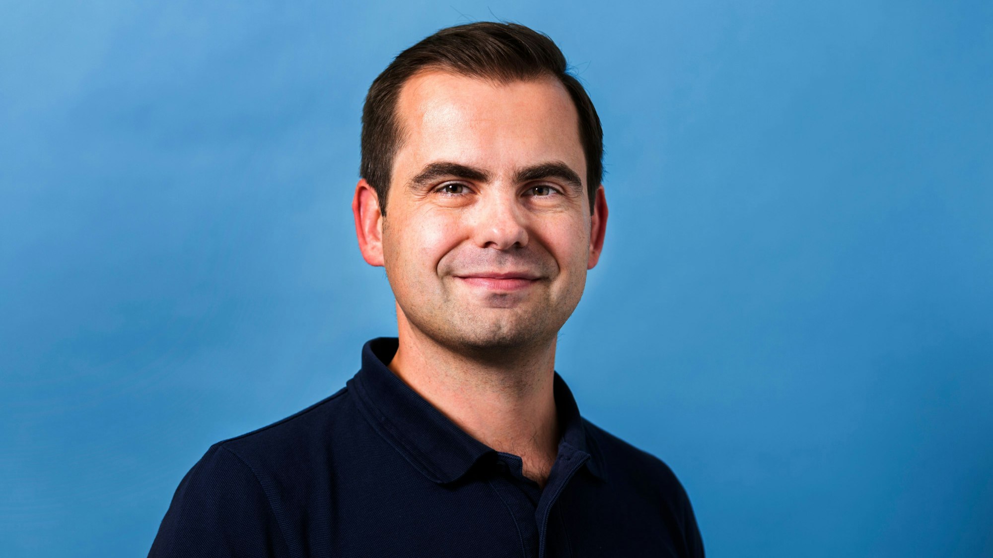 Jaroslaw Kutylowski steht vor einem blauen Hintergrund.