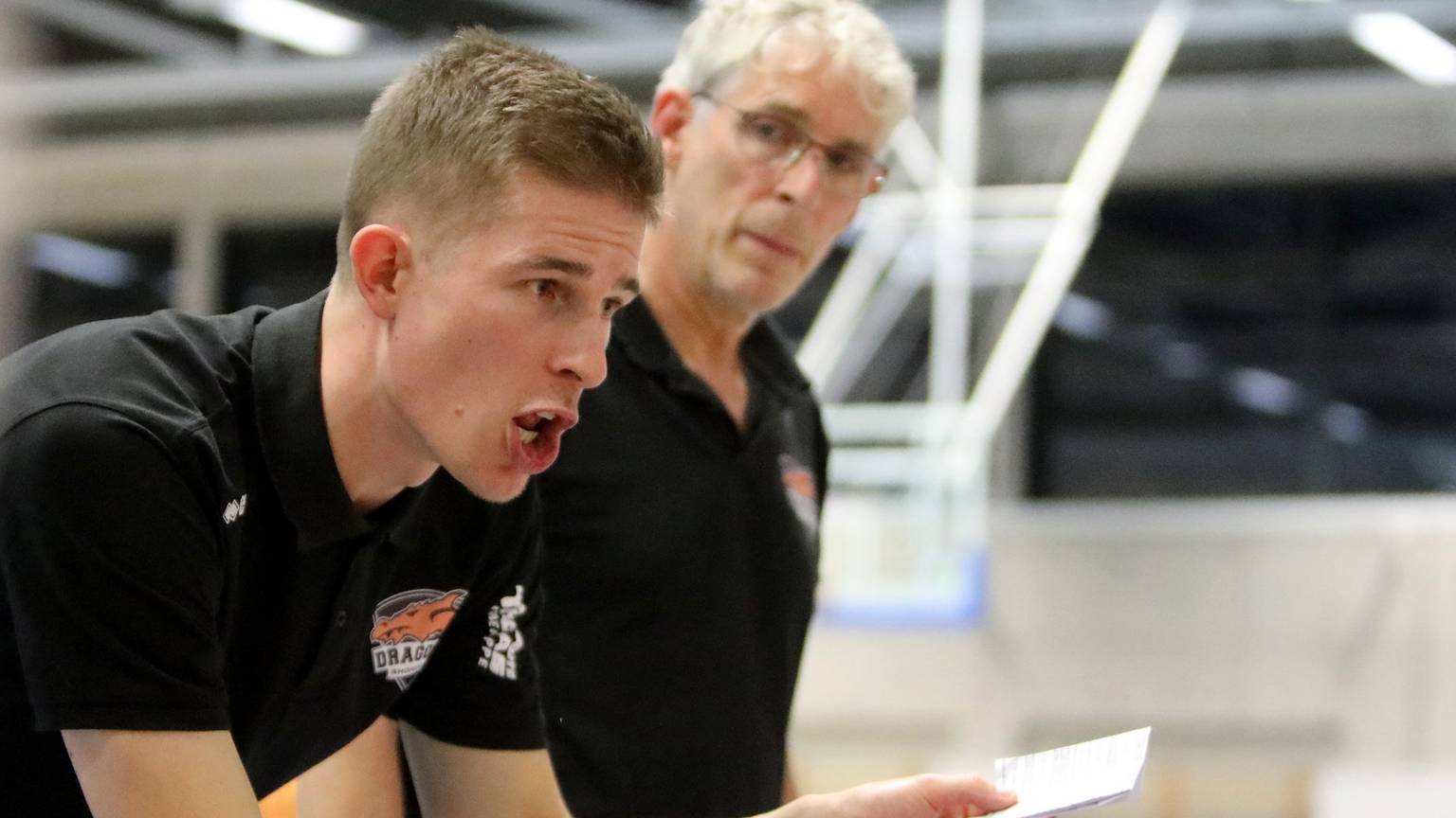 Der Rhöndorfer Cheftrainer Julius Thomas (vorne) hält einen Zettel in der Hand und instruiert seine Spieler. Co-Trainer Martin Otto hört aufmerksam zu.