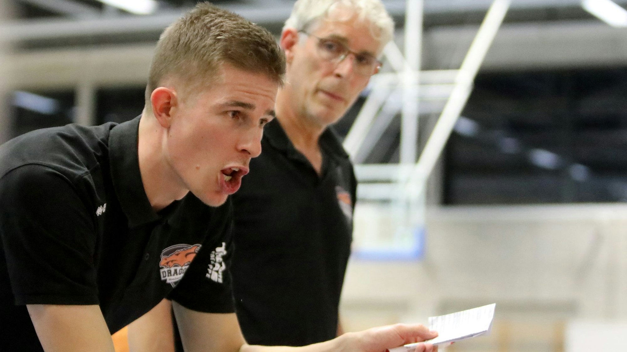 Der Rhöndorfer Cheftrainer Julius Thomas (vorne) hält einen Zettel in der Hand und instruiert seine Spieler. Co-Trainer  Martin Otto hört aufmerksam zu.