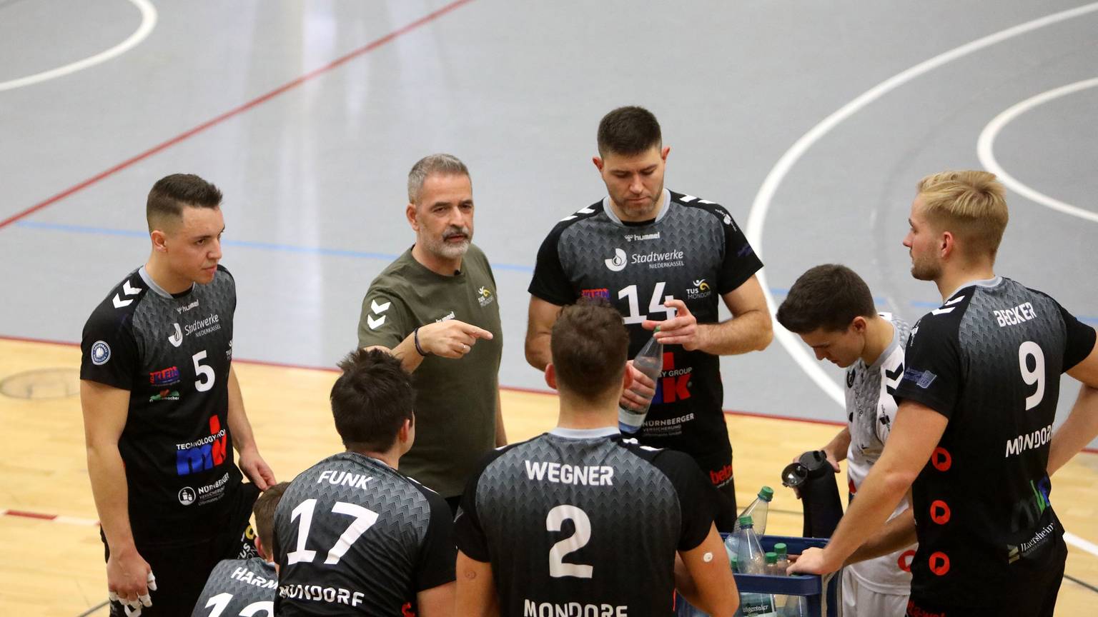 Cheftrainer Tasos Vlasakidis vom TuS Mondorf macht Ansagen und gestikuliert, seine Spieler hören gespannt zu.